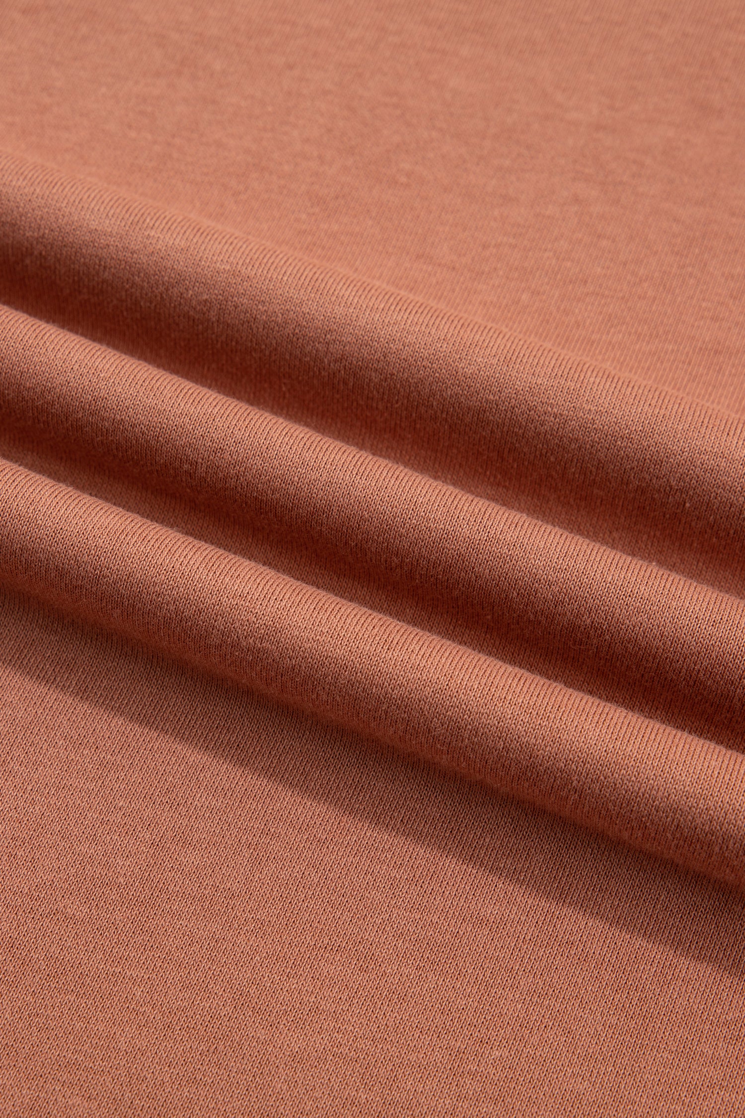 A close-up of draped ribbed knit fabric in a warm terracotta or rust color, showing the texture and folds.