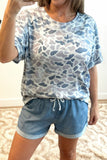 Person wearing a blue and white patterned shirt and denim shorts indoors.