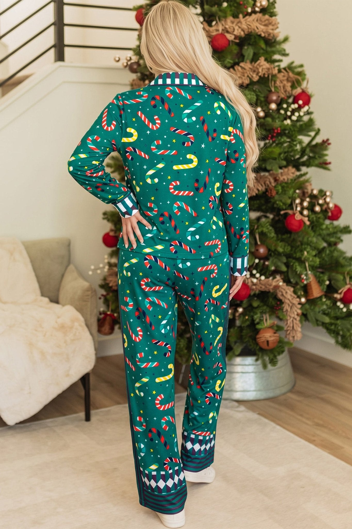Back view of woman in colorful candy cane Christmas pajamas beside decorated tree.