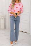Person wearing a pink sweater with red heart patterns and blue jeans, holding a coffee cup.