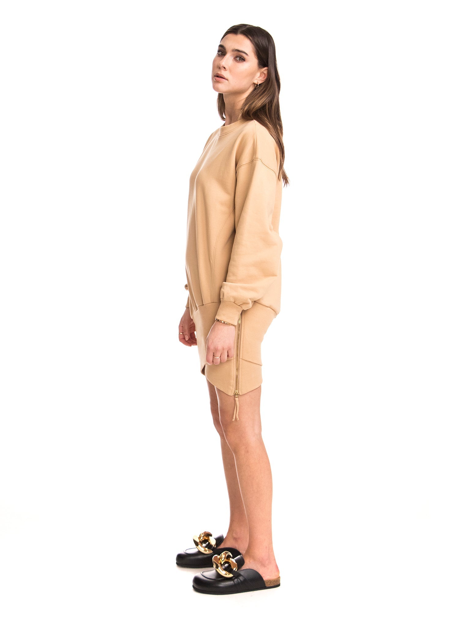 Woman wearing a beige outfit with black sandals on a white background