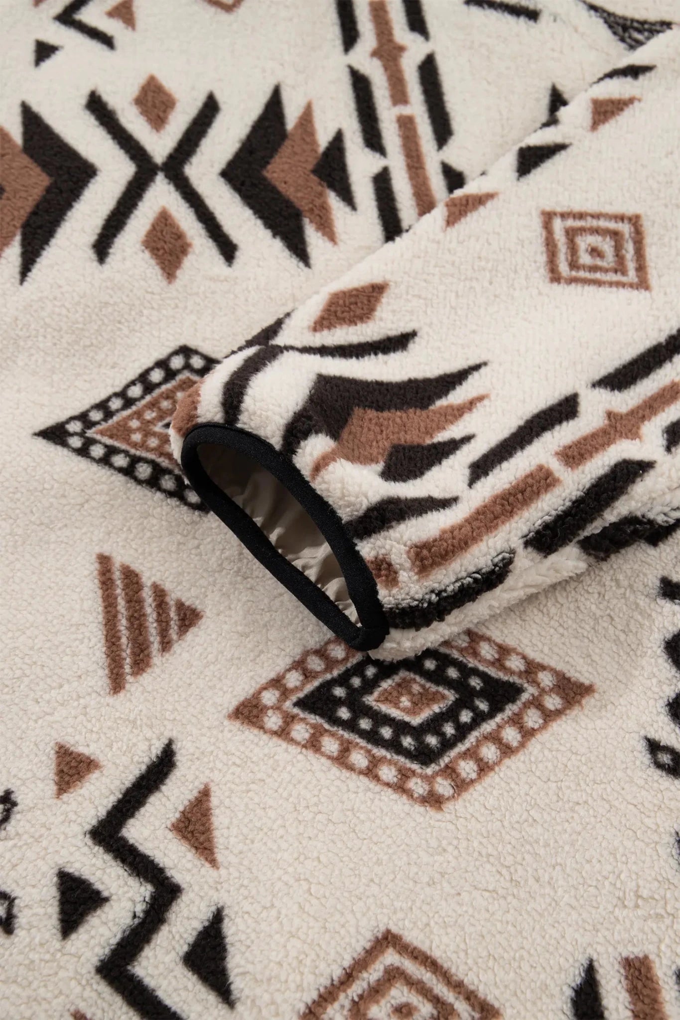 A close-up of a fleece blanket with a Southwestern geometric pattern in black, brown, and cream.