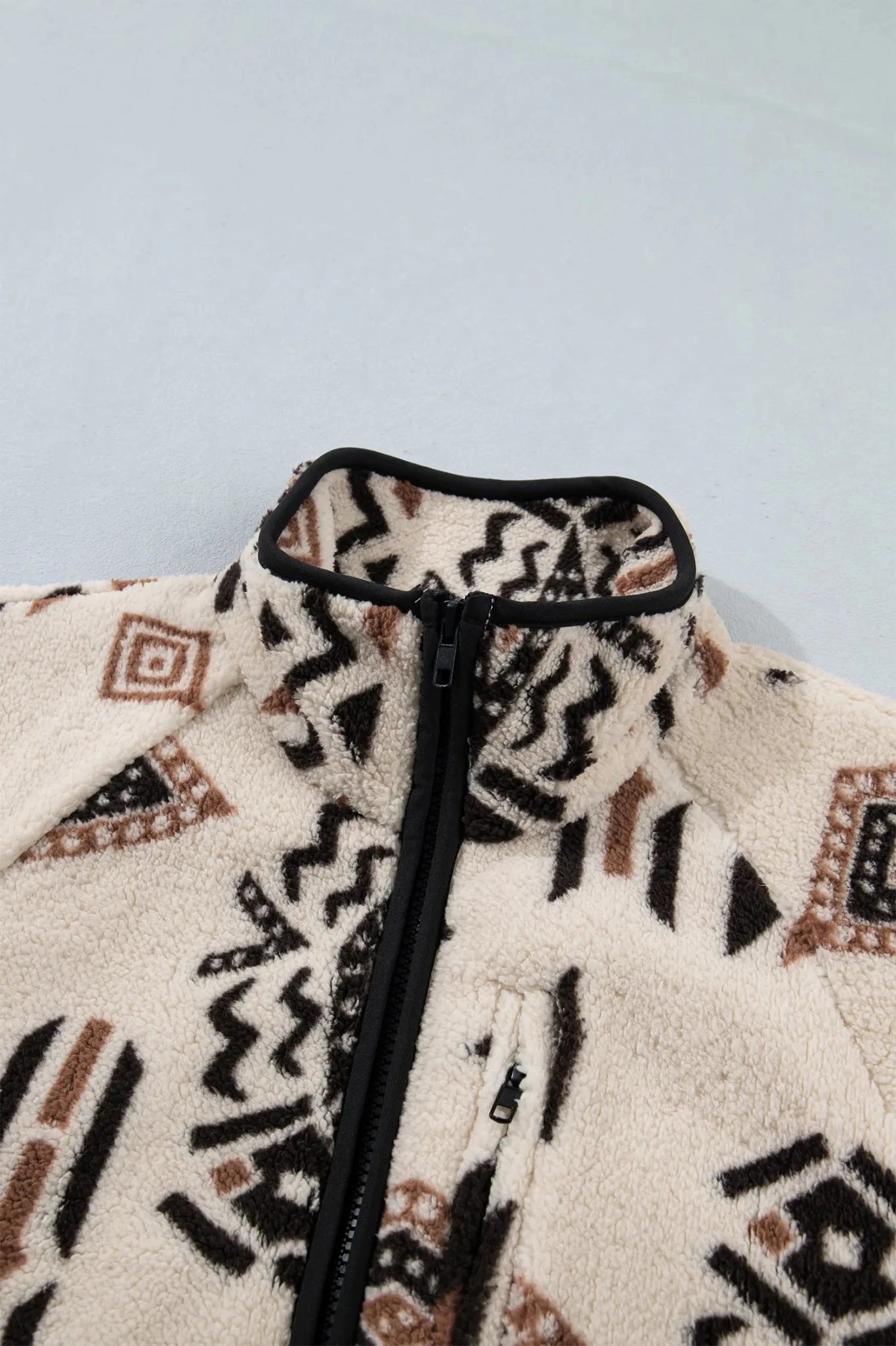 Close-up of a fleece zip-up jacket with a high collar, featuring a cream base with black and brown geometric patterns.