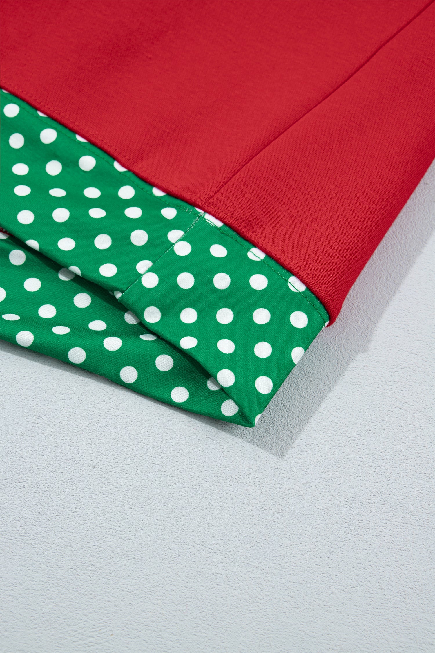 Folded fabric showing solid red top layer and green layer with white polka dots on a light gray surface.