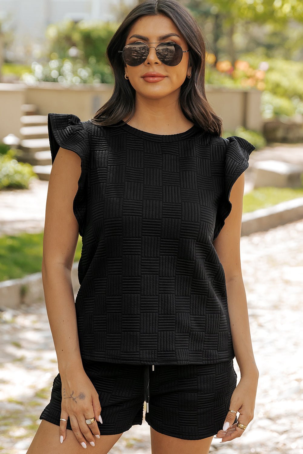 Woman wearing a black sleeveless top and shorts outdoors.