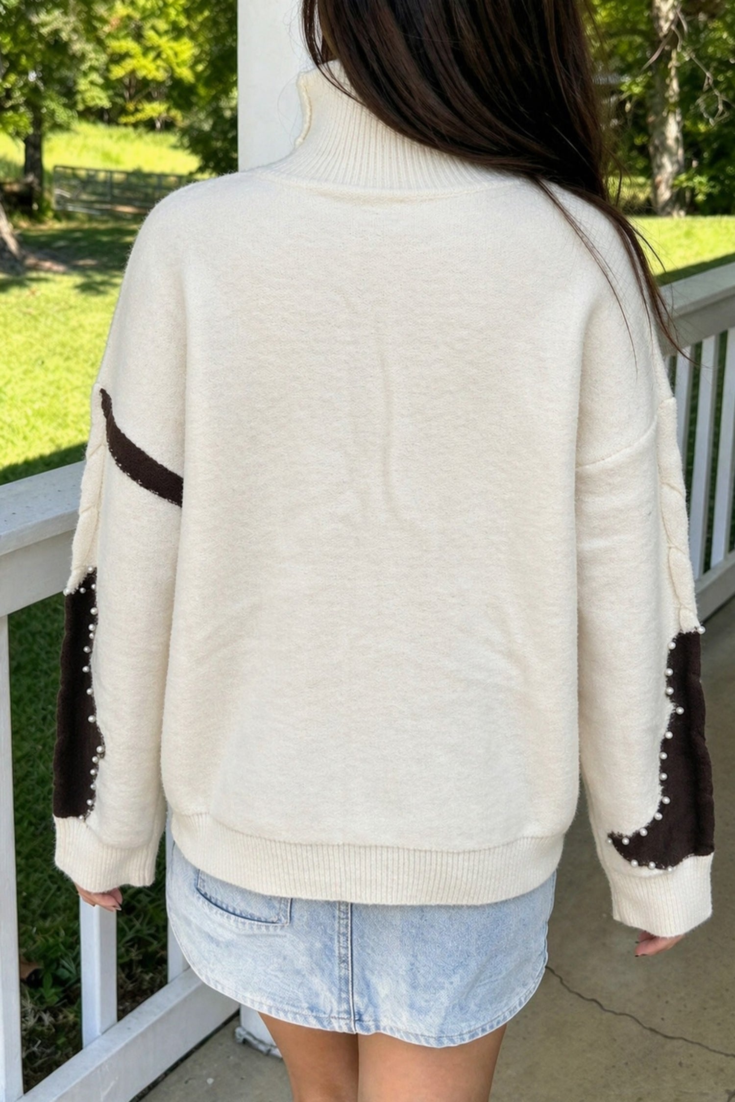 Back view of beige mock neck sweater with brown cow spot sleeve patches