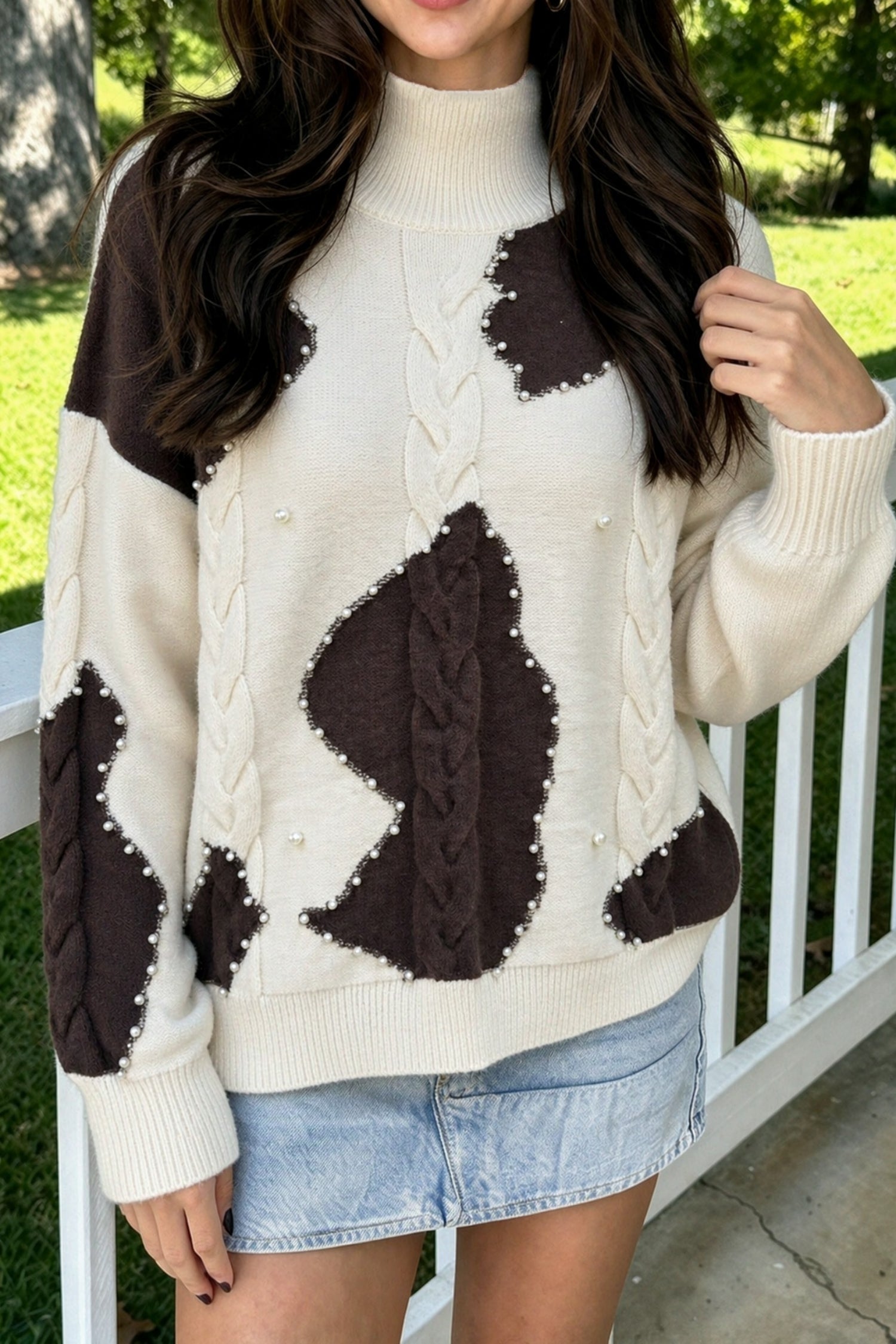 Beige cow print cable knit sweater with pearl bead trim, worn with a light denim mini skirt