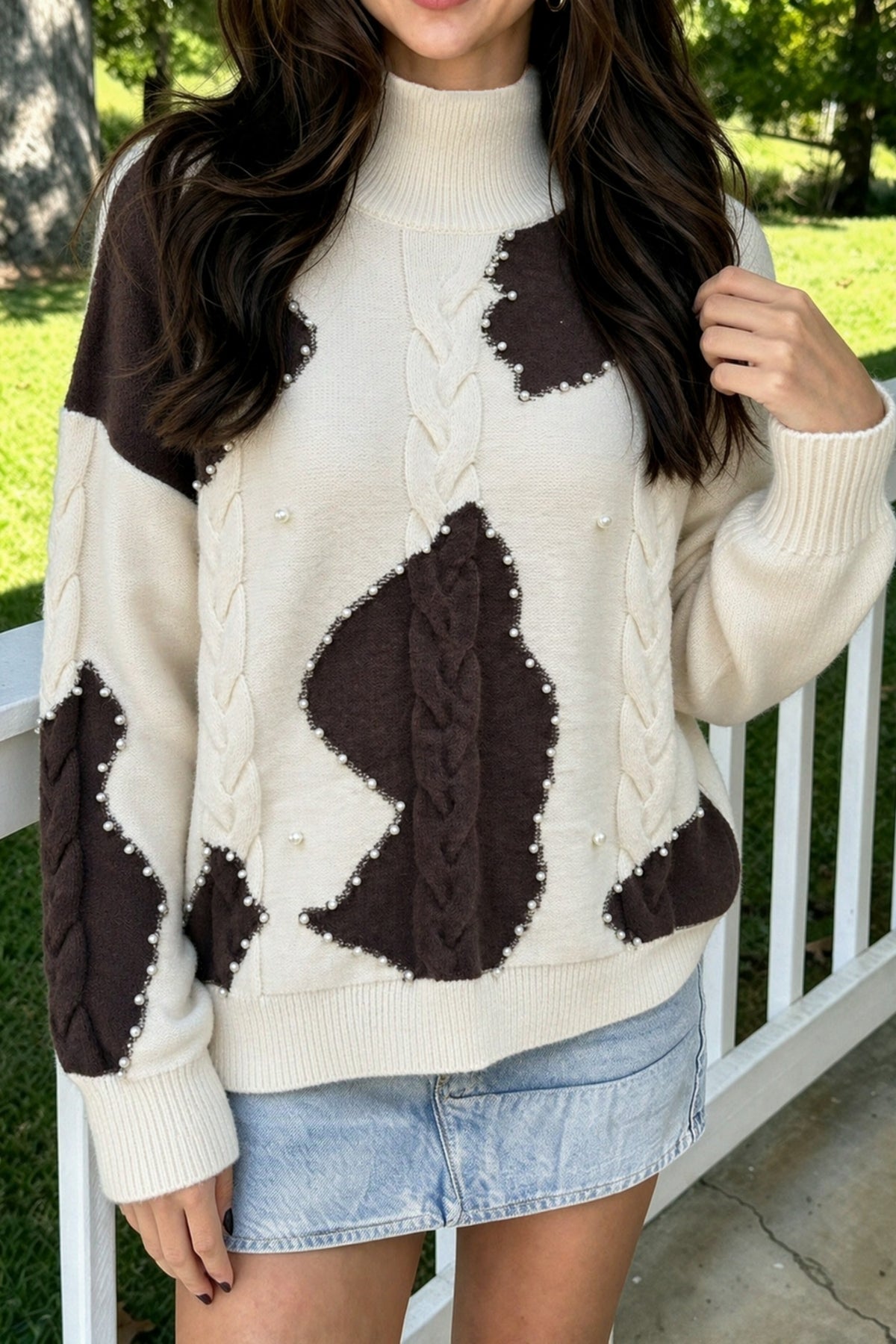 Beige cow print cable knit sweater with pearl bead trim, worn with a light denim mini skirt