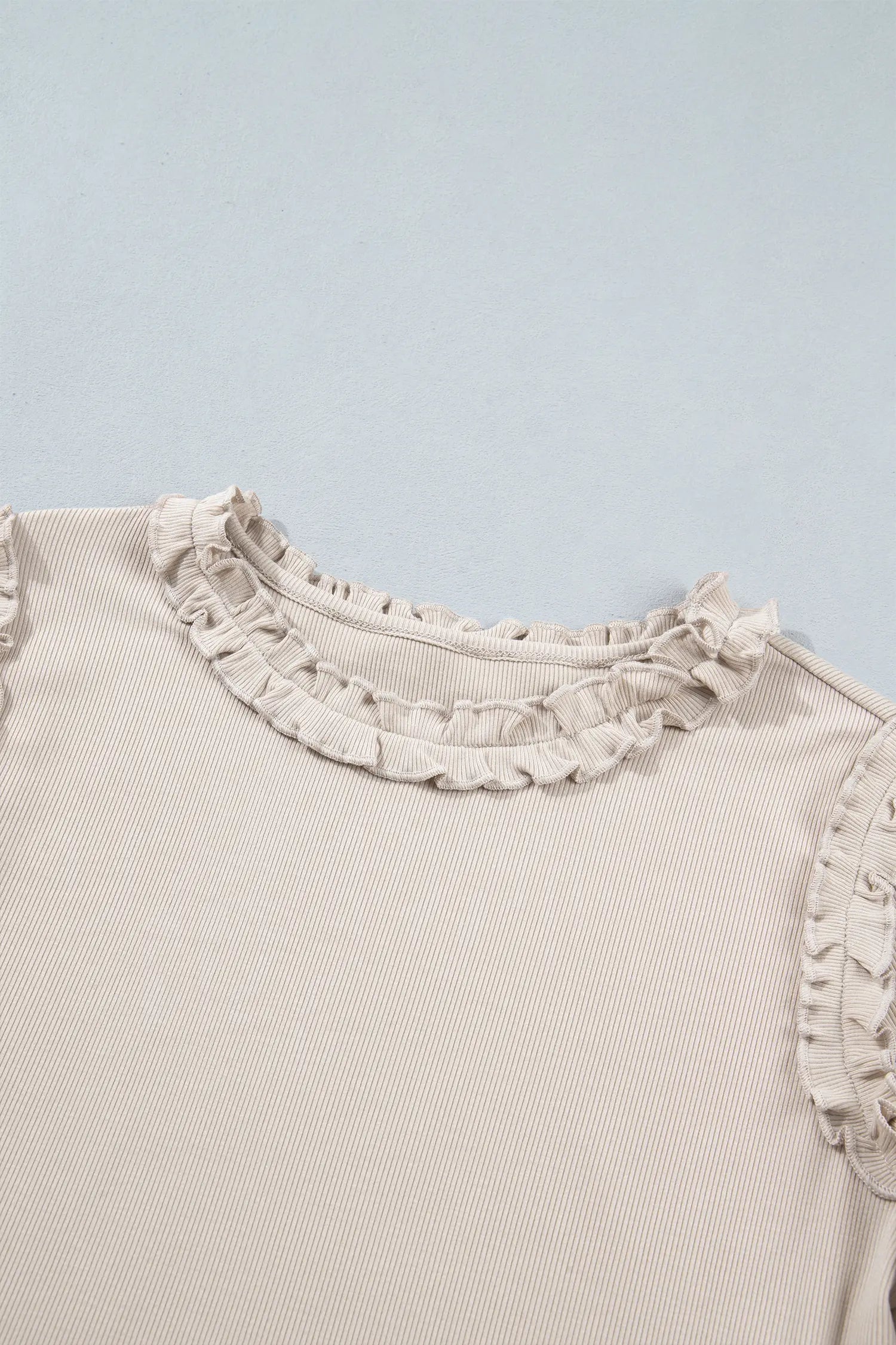 Close-up of frill trim round neckline on beige ribbed knit top