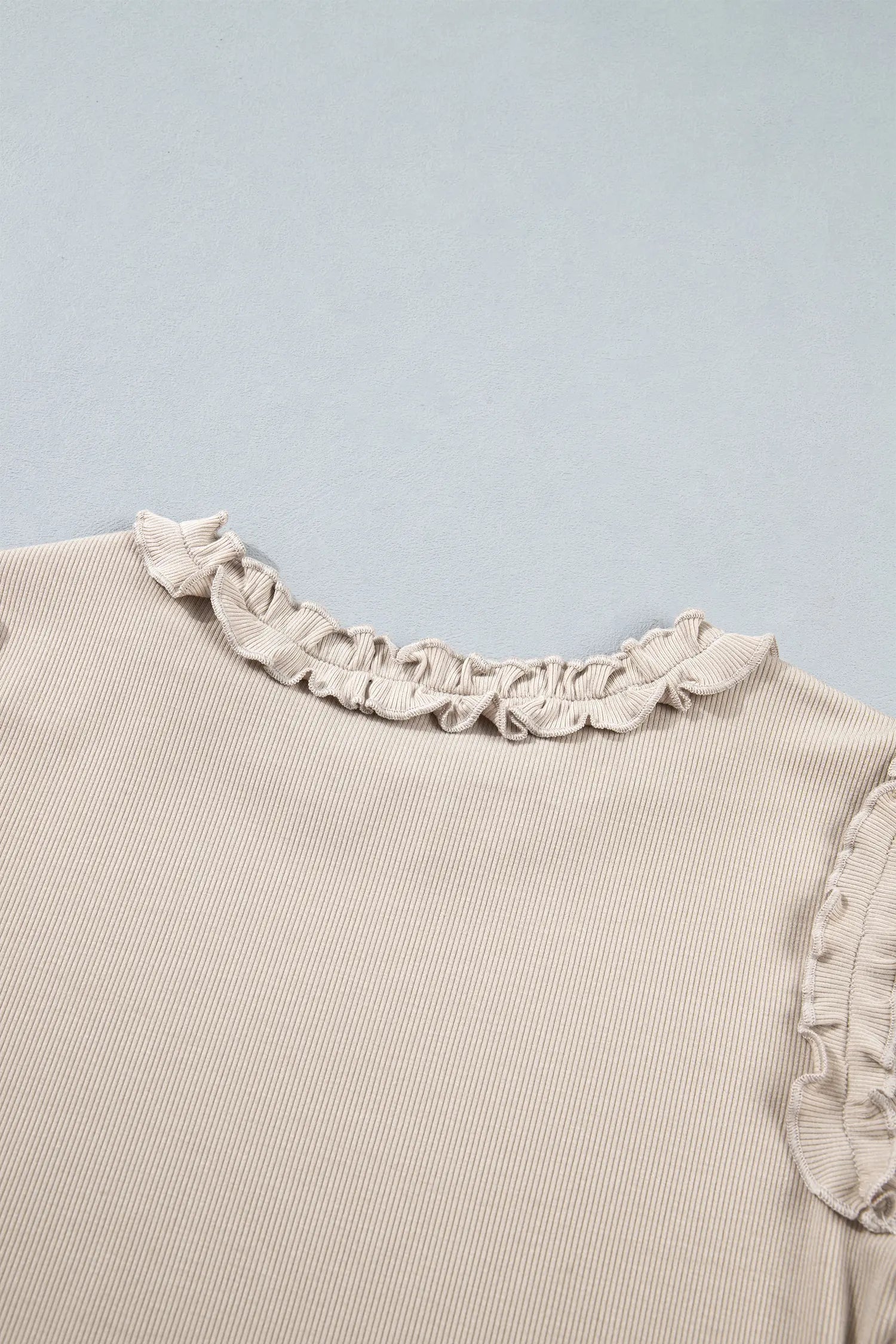 Close-up of frill trim on neckline and shoulder seam of beige ribbed top
