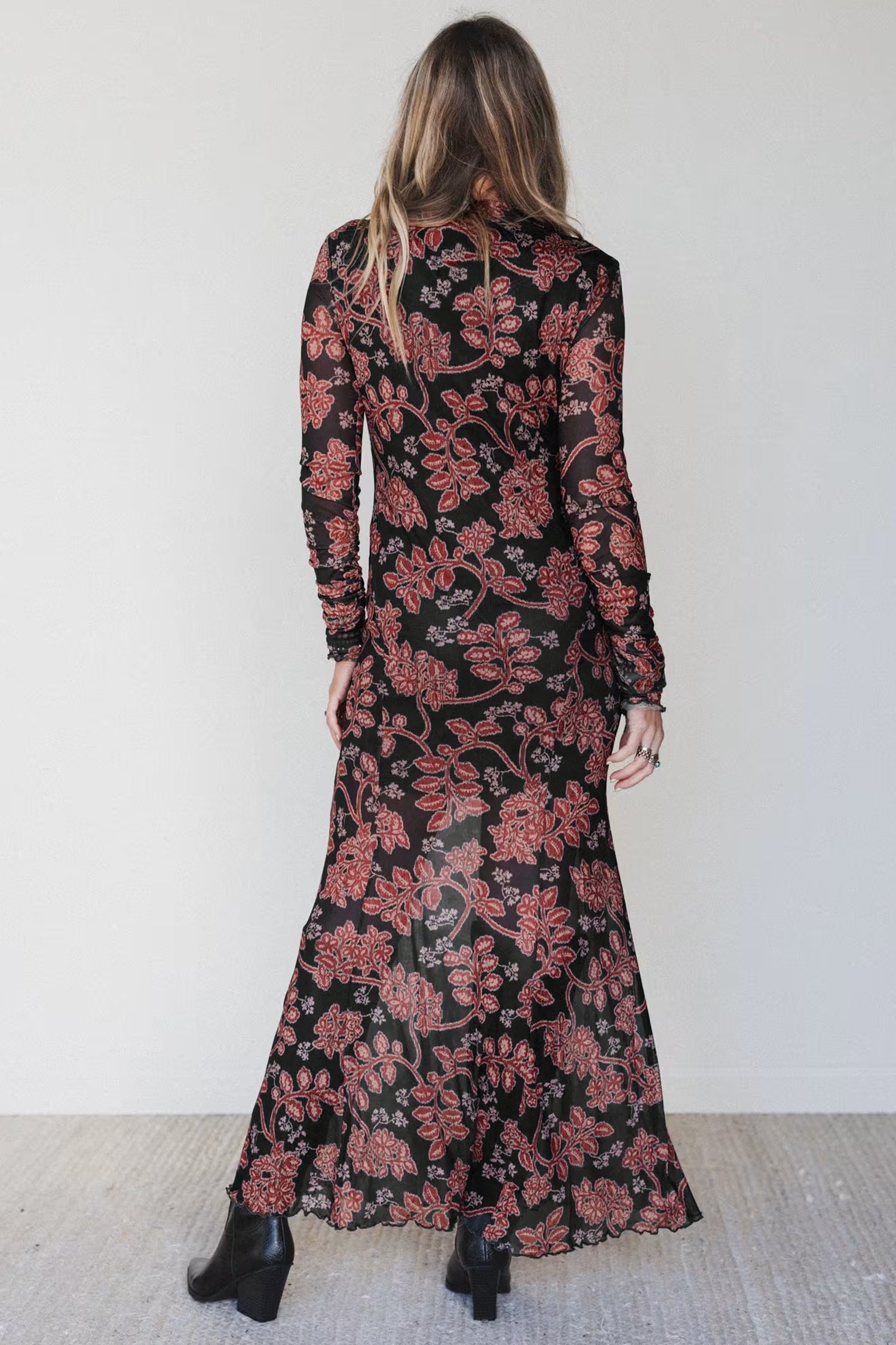 Back view of fitted black floral mesh maxi dress against a white wall