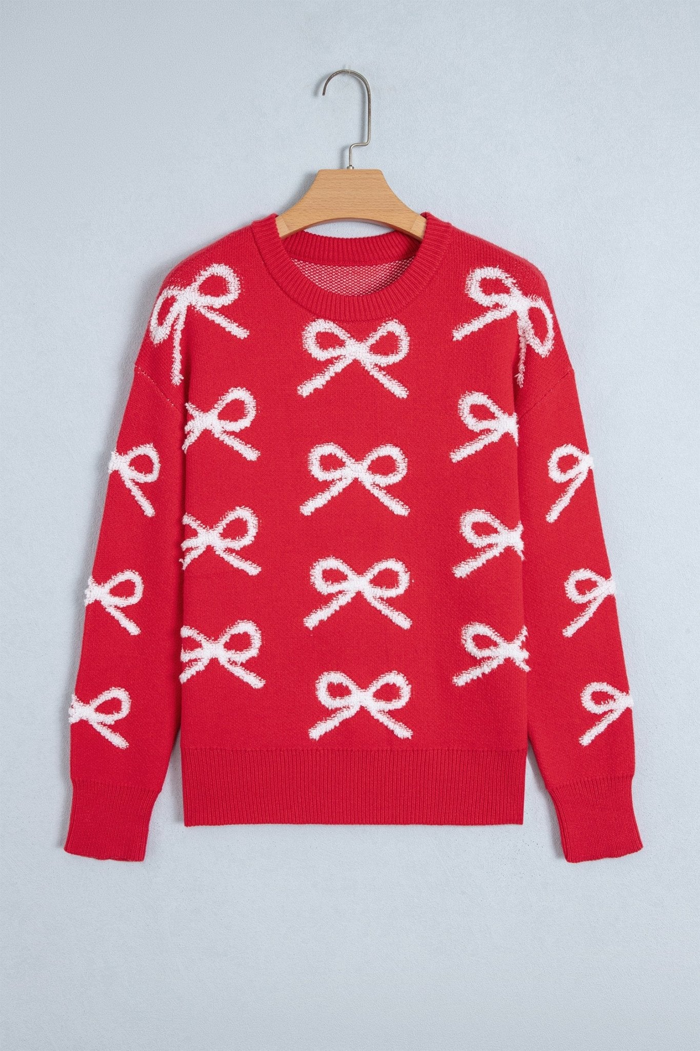 Red crewneck knit sweater with repeating white bow pattern on wooden hanger.