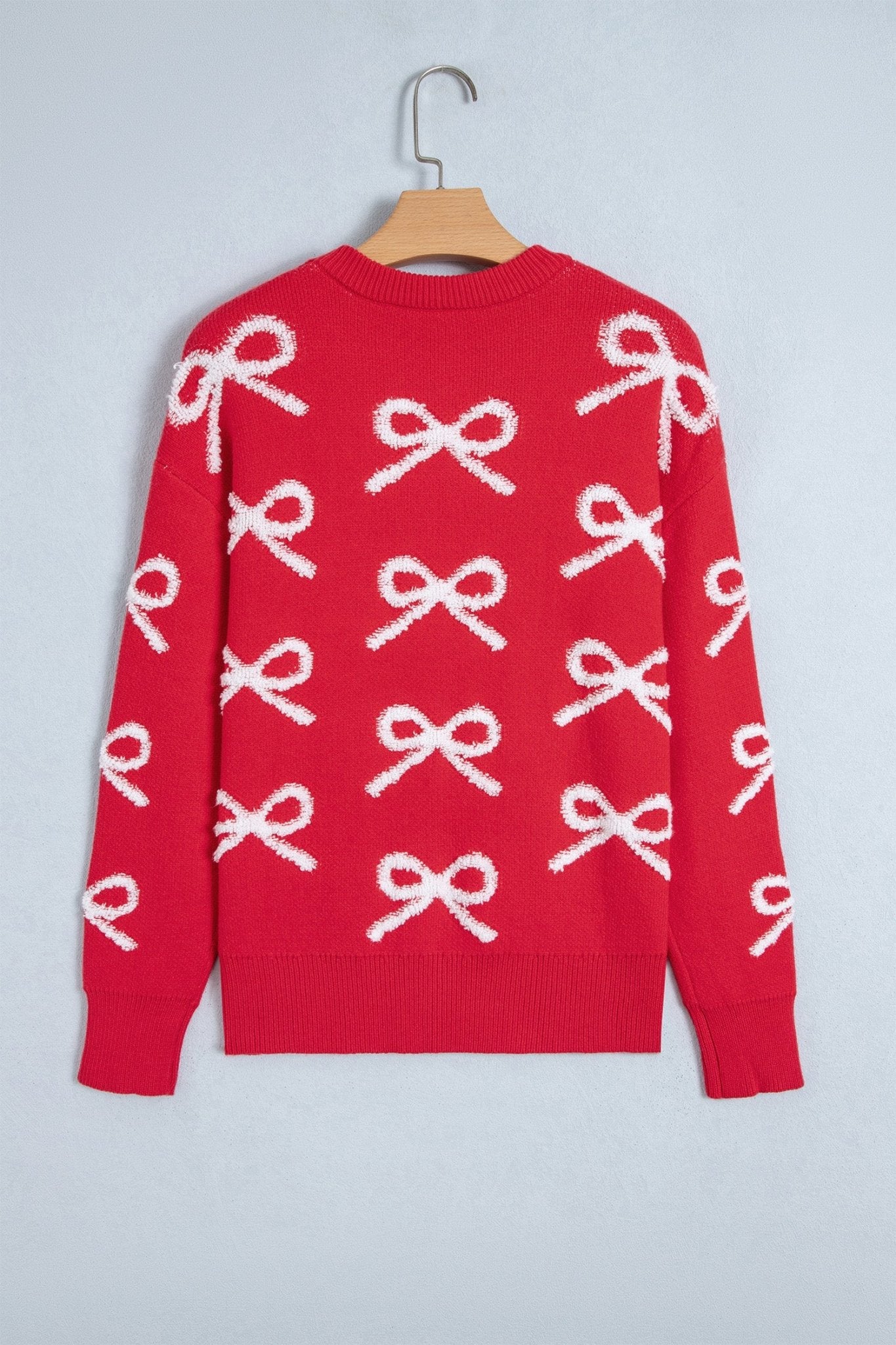Red crewneck sweater with repeating white knit bow pattern on wooden hanger.