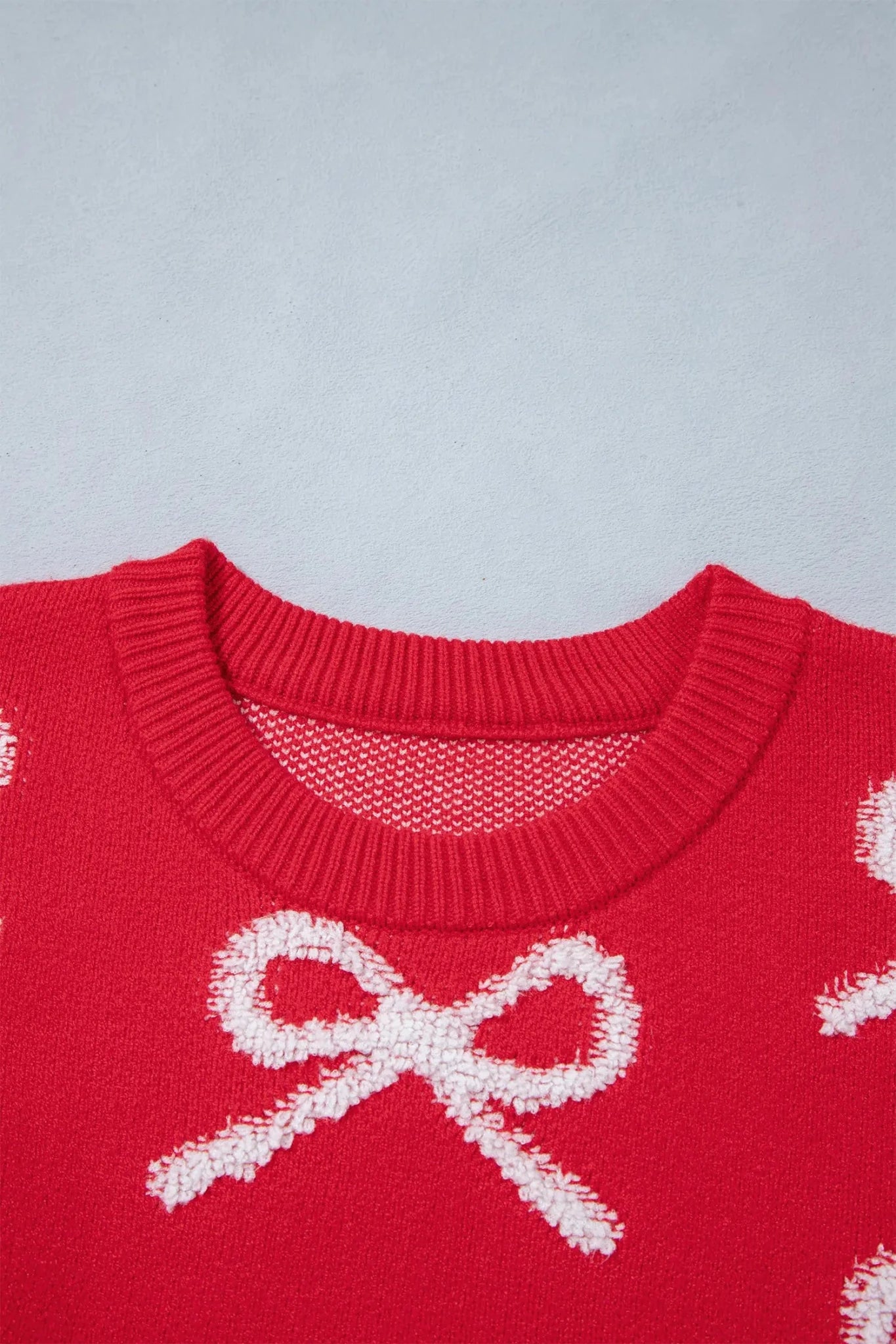 Close-up of red knit sweater featuring a white knitted bow pattern.