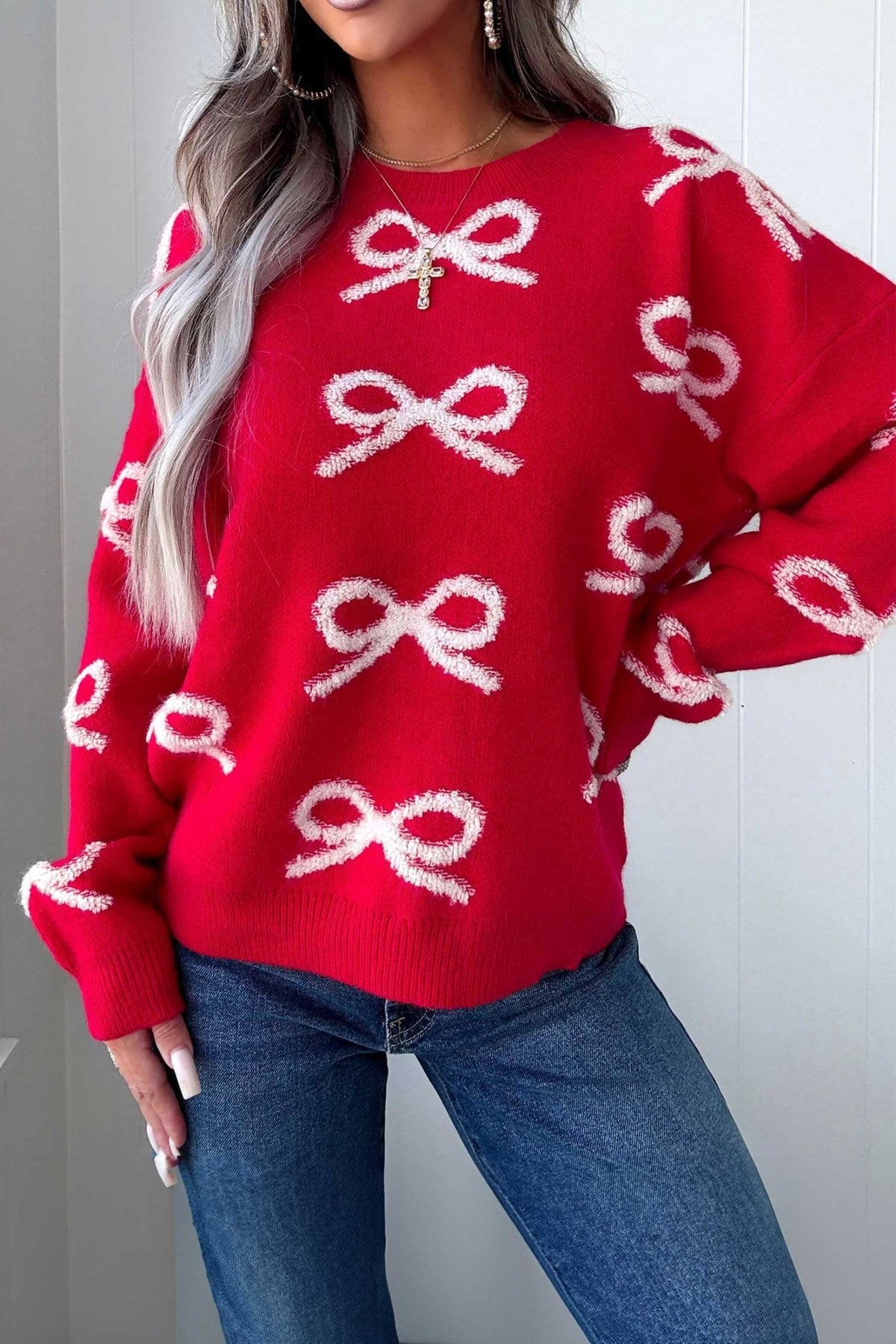 Woman in bright red knit sweater with white bow pattern and blue jeans.