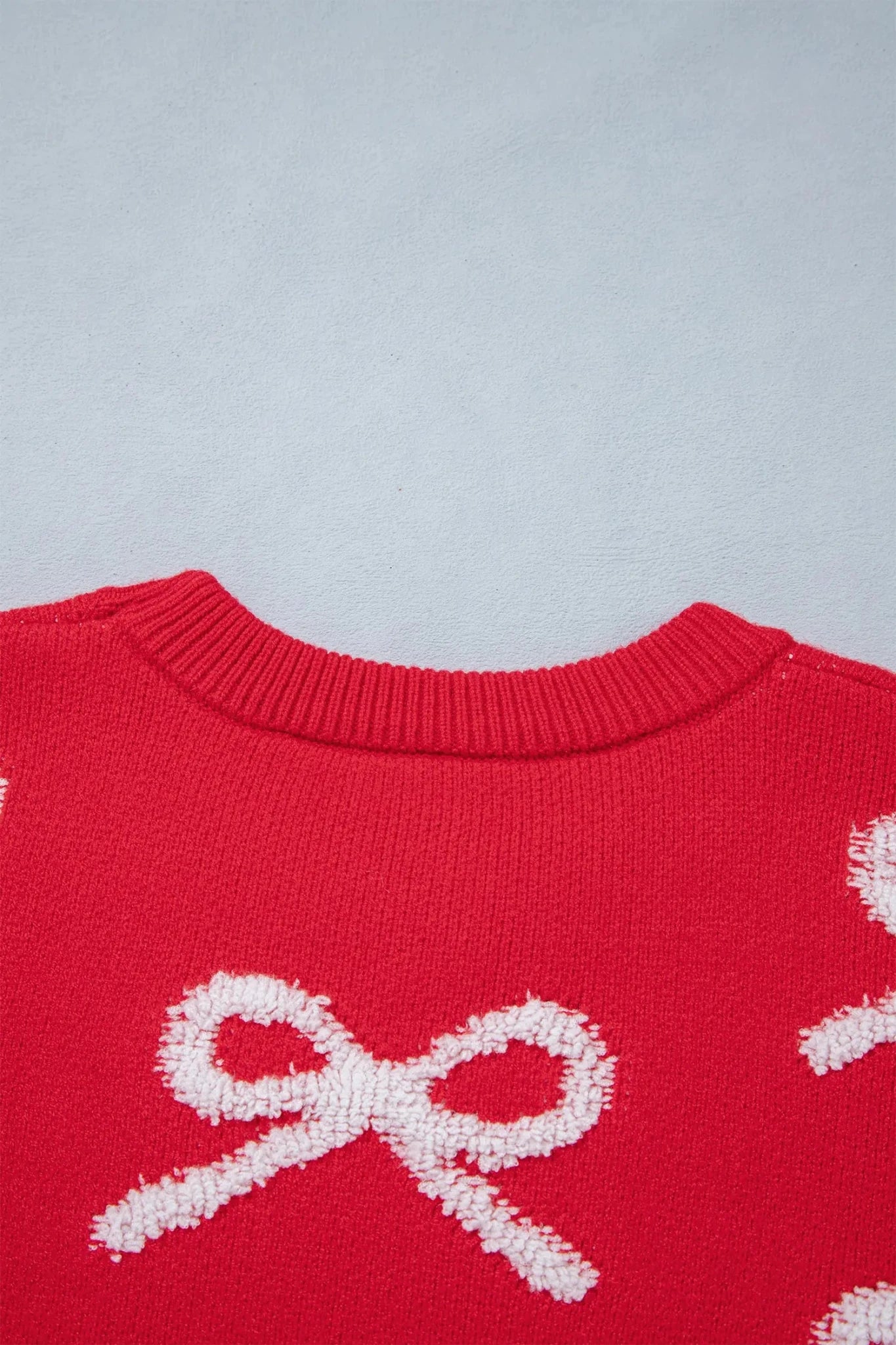 Close-up of red knit sweater with textured white knitted bow motifs.