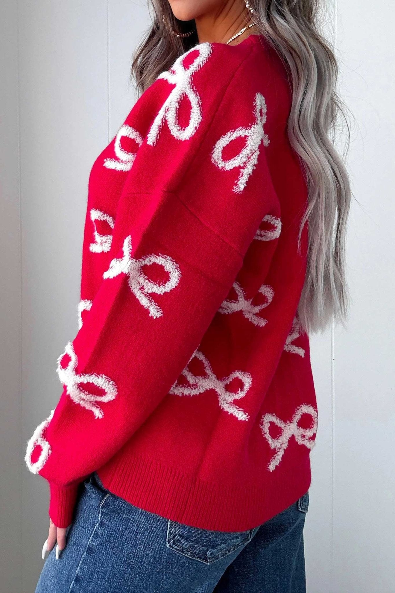 Side-back view of woman in bright red knit sweater with white fuzzy bow patterns and jeans.