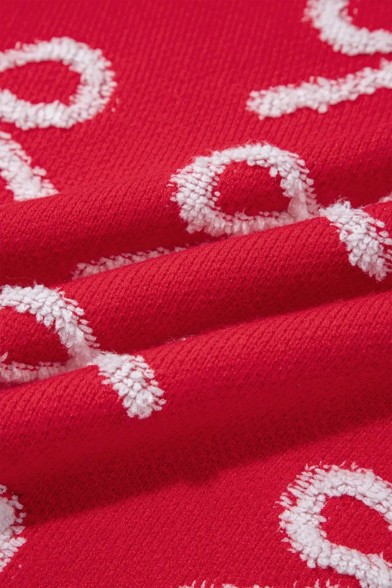 Close-up of red knit fabric with repeating white textured letterform pattern.