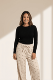 Woman wearing a black top and beige patterned pants against a neutral background