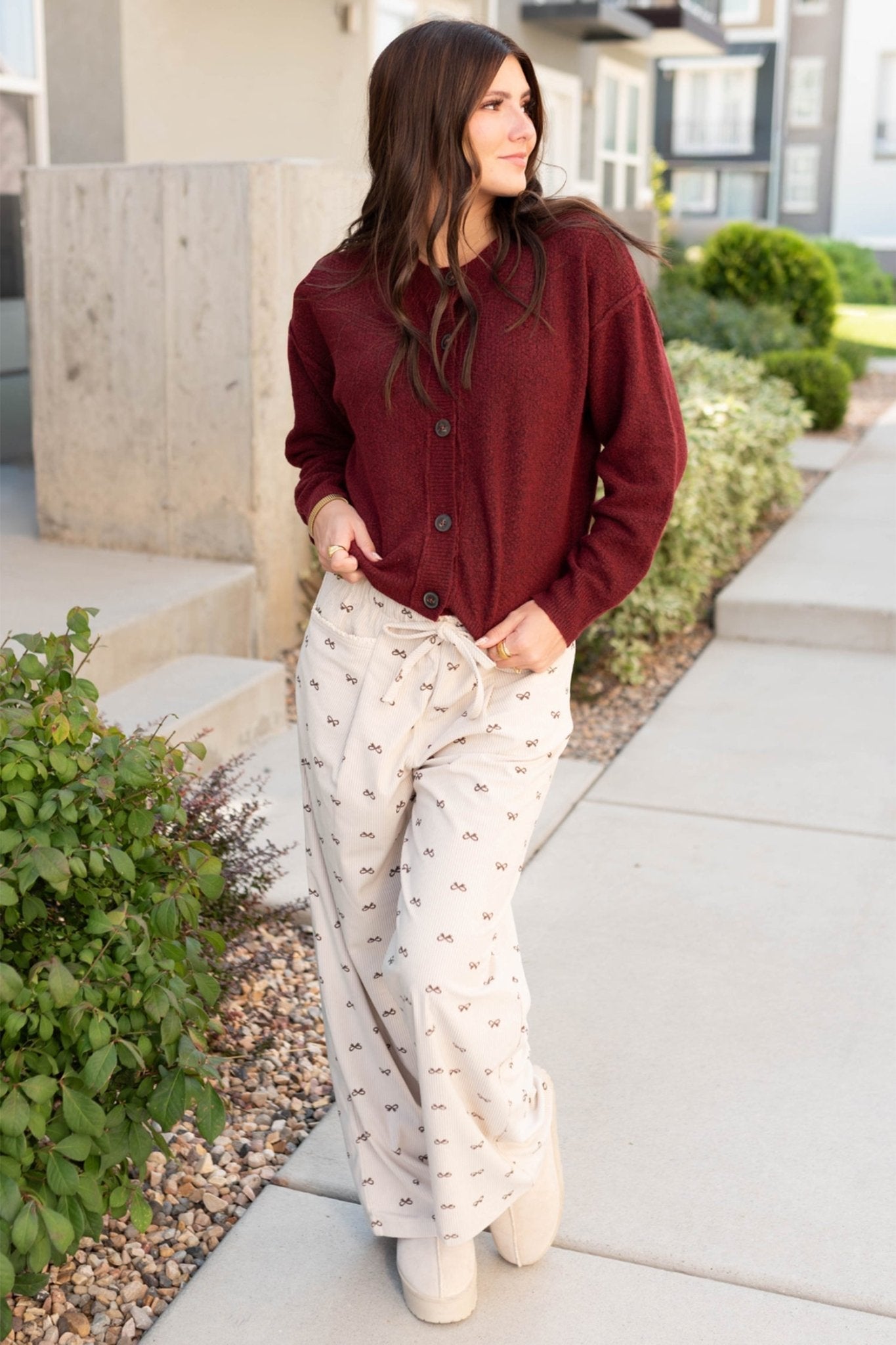 Woman wearing a red jacket and white patterned pants standing on a sidewalk.