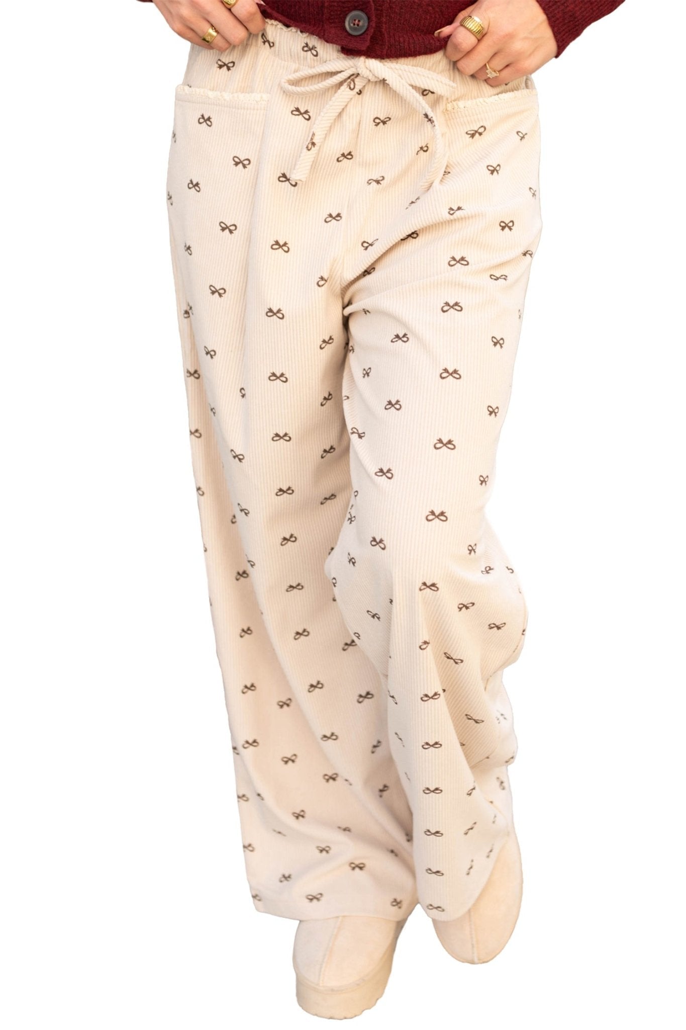 Beige pajama pants with bow pattern worn by a person on a white background