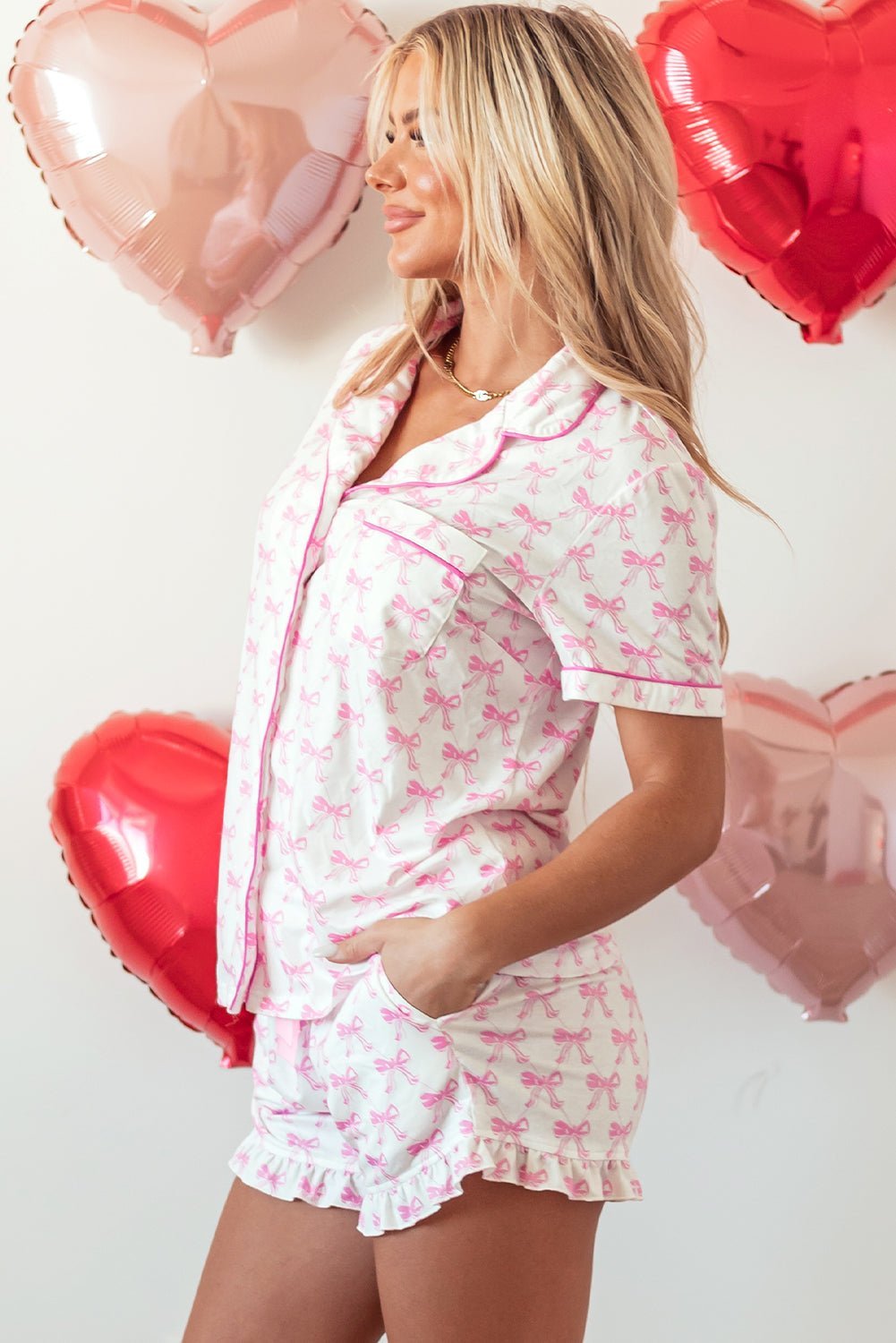Woman wearing a pink and white pajama set with heart-shaped balloons in the background.