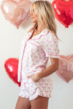 Woman wearing a pink and white pajama set with heart-shaped balloons in the background.