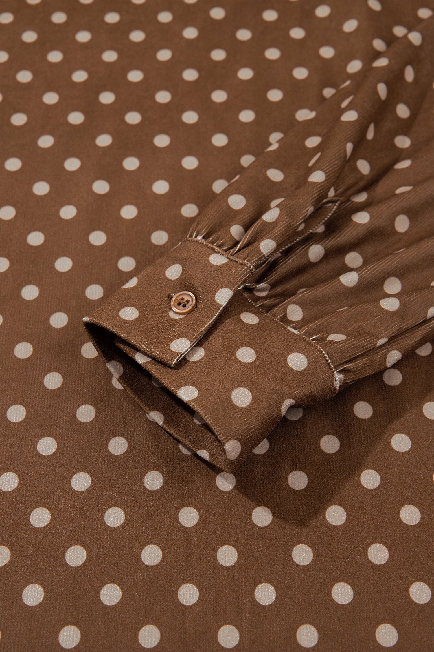 Close-up of gathered button cuff on brown polka dot long sleeve dress