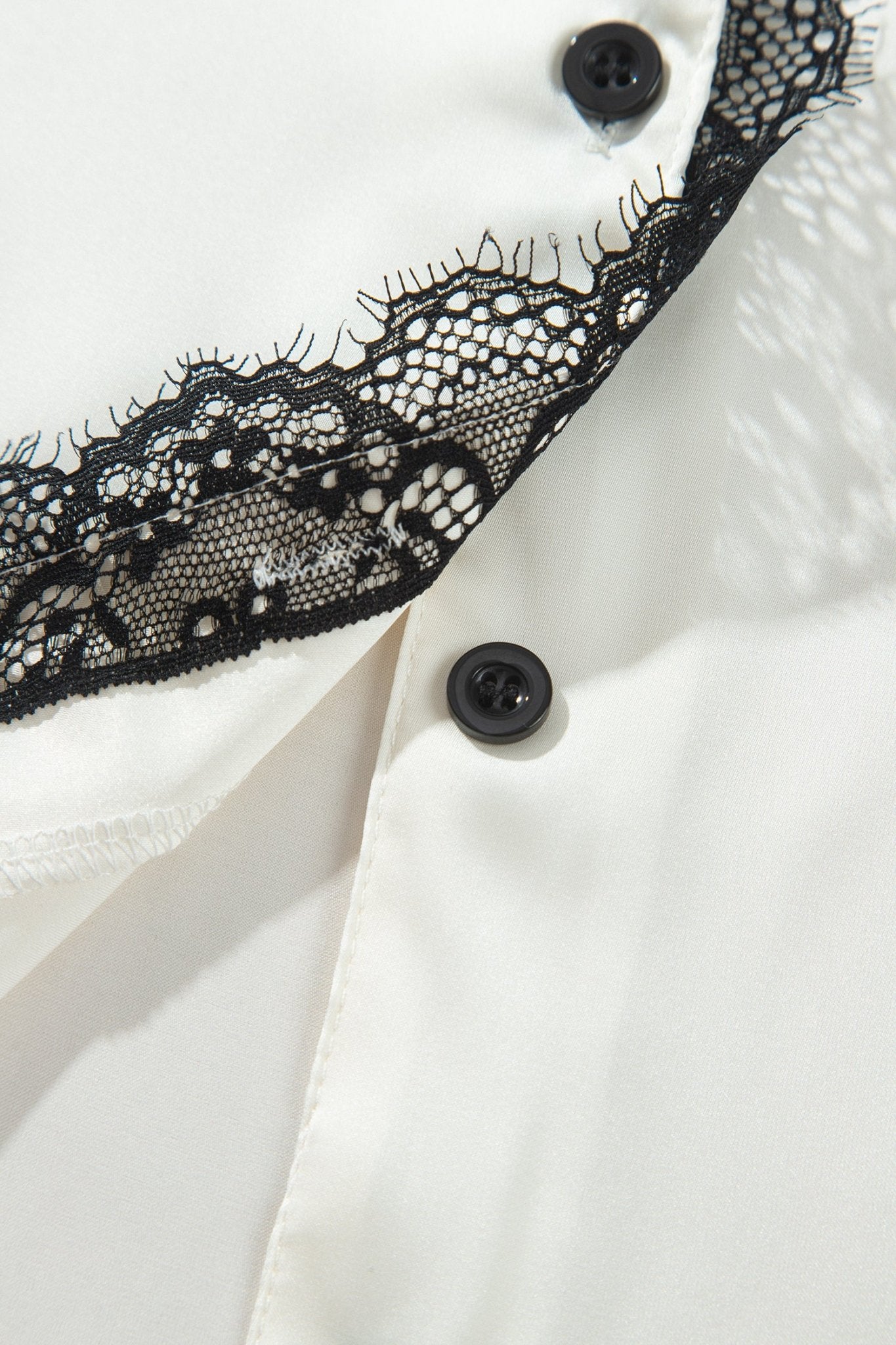 Close-up of a white shirt with black lace trim along the collar and black buttons.