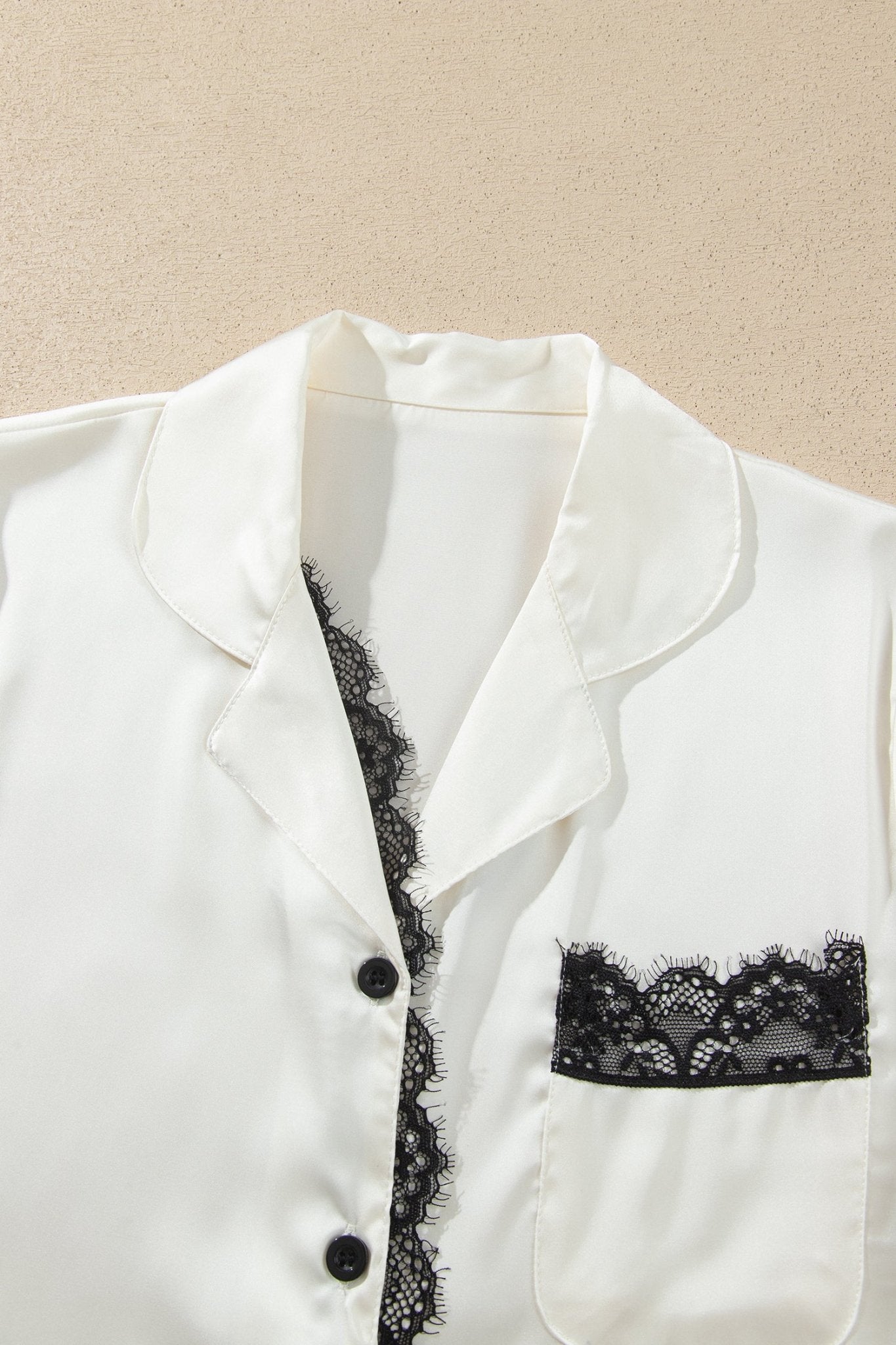 White satin pajama shirt with black lace trim, pocket, and buttons.