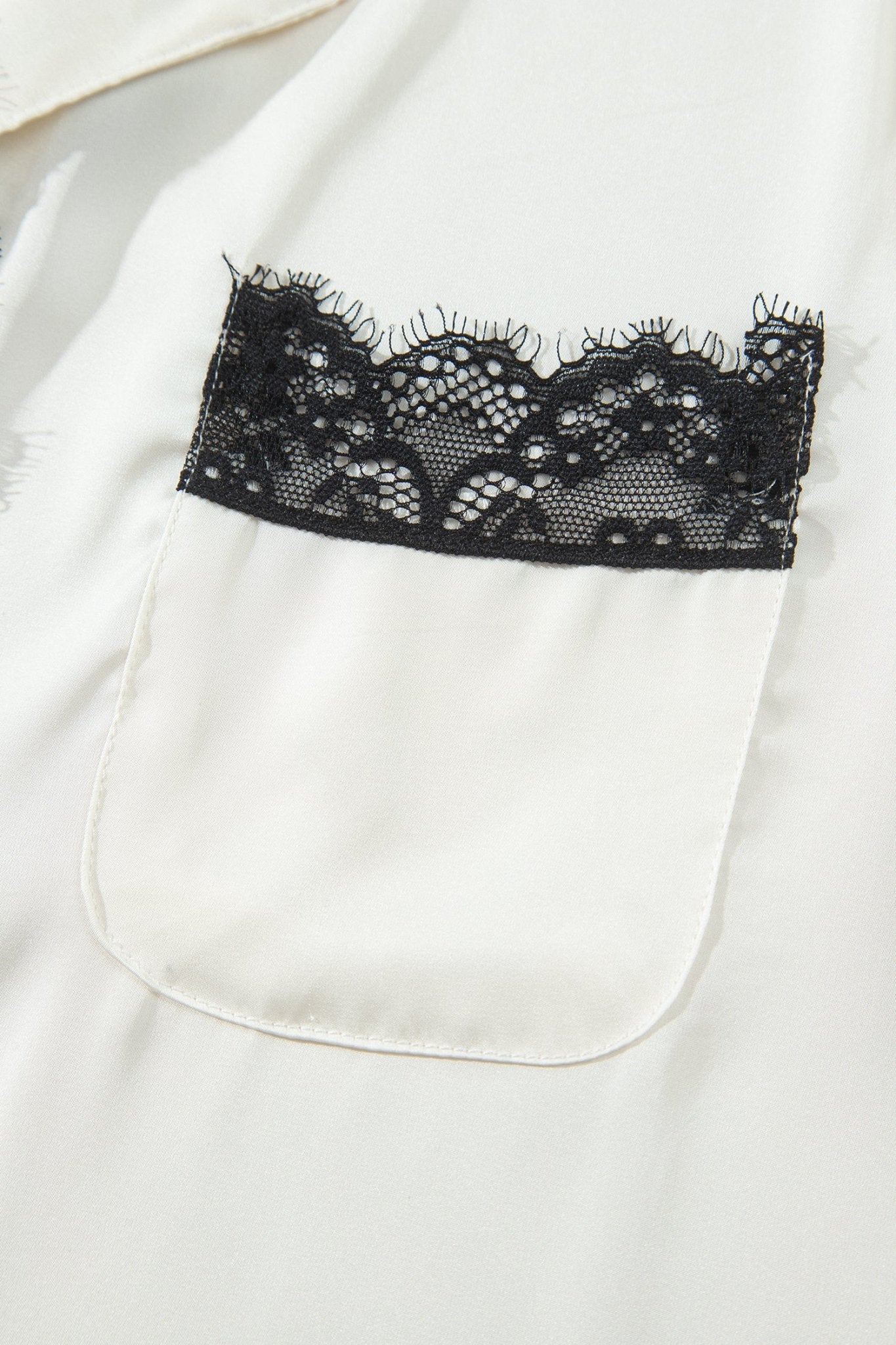 Close-up of white garment with patch pocket and decorative black lace trim.