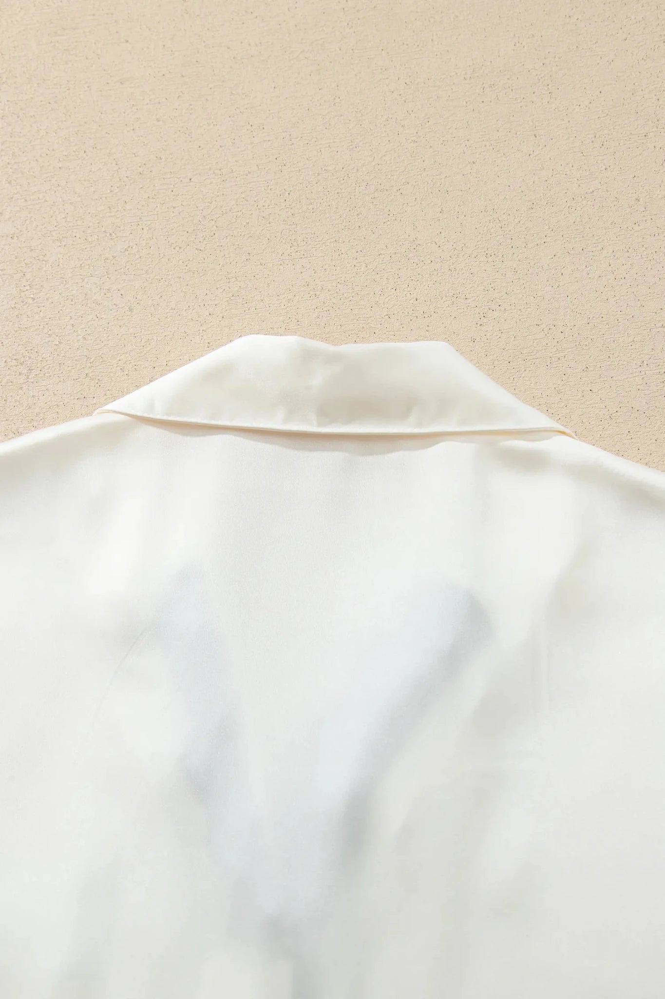 Close-up of a white satin or silk shirt collar against a textured beige background.