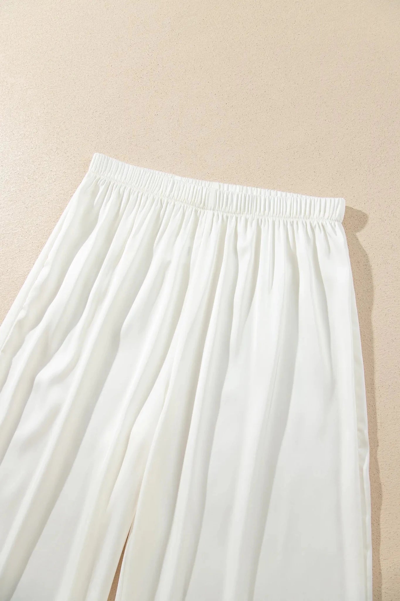 Close-up of white wide-leg trousers with elastic waistband.
