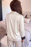 Back view of woman in cream satin pajamas with black lace cuffs.