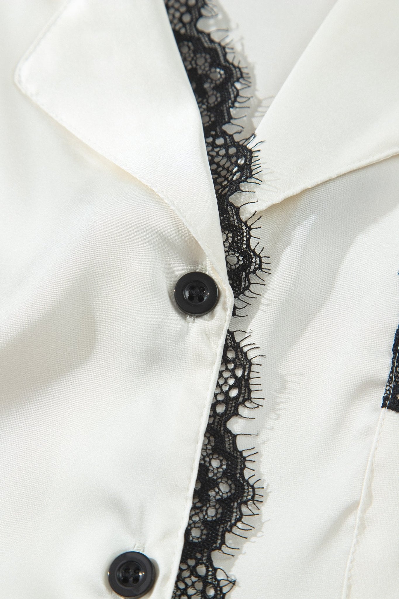 Close-up of a white satin-like collared garment with black lace trim and black buttons.