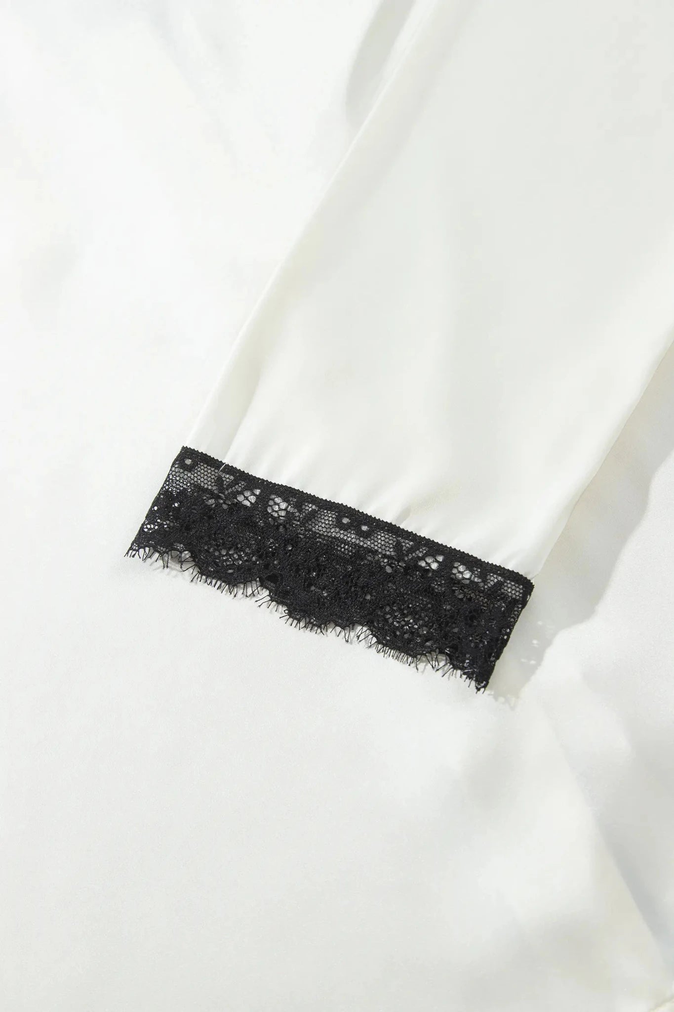 Close-up of a white garment with a black lace trim detail along the cuff.