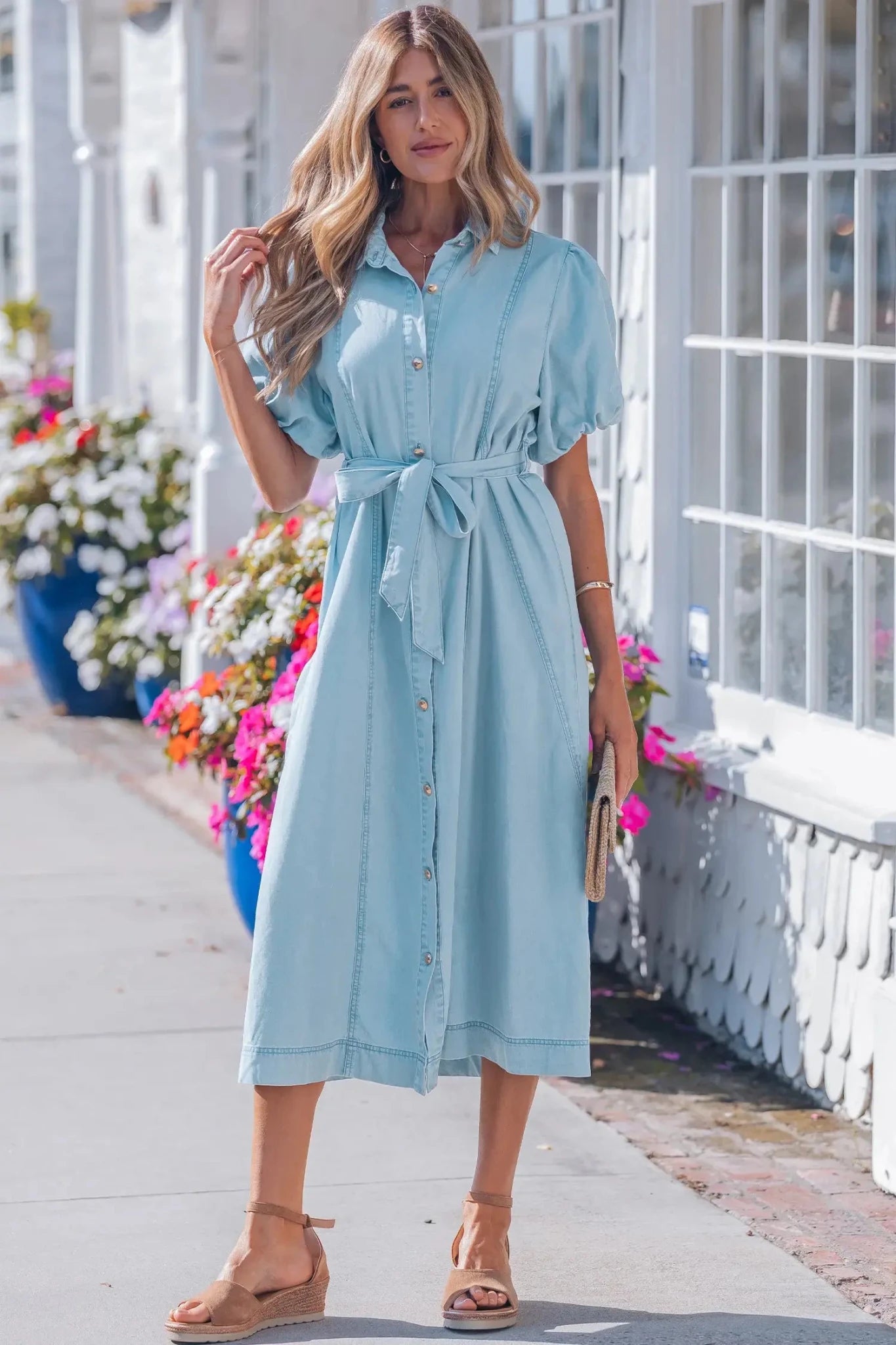 Woman wearing a light blue dress standing on a sidewalk with flowers in the background
