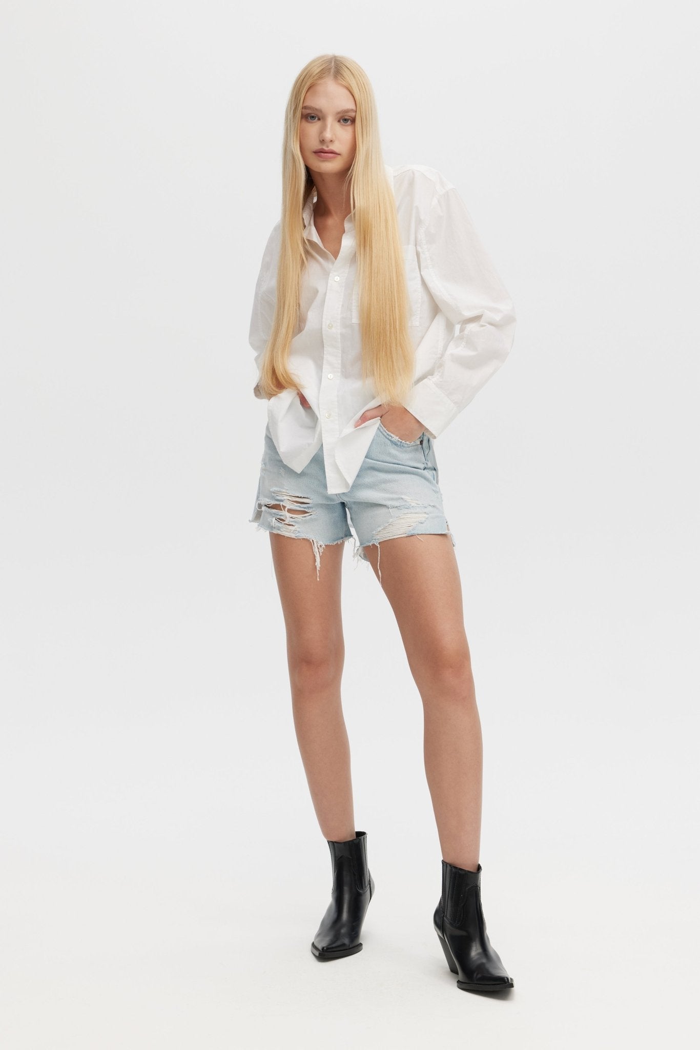 Woman wearing a white shirt, denim shorts, and black boots on a white background