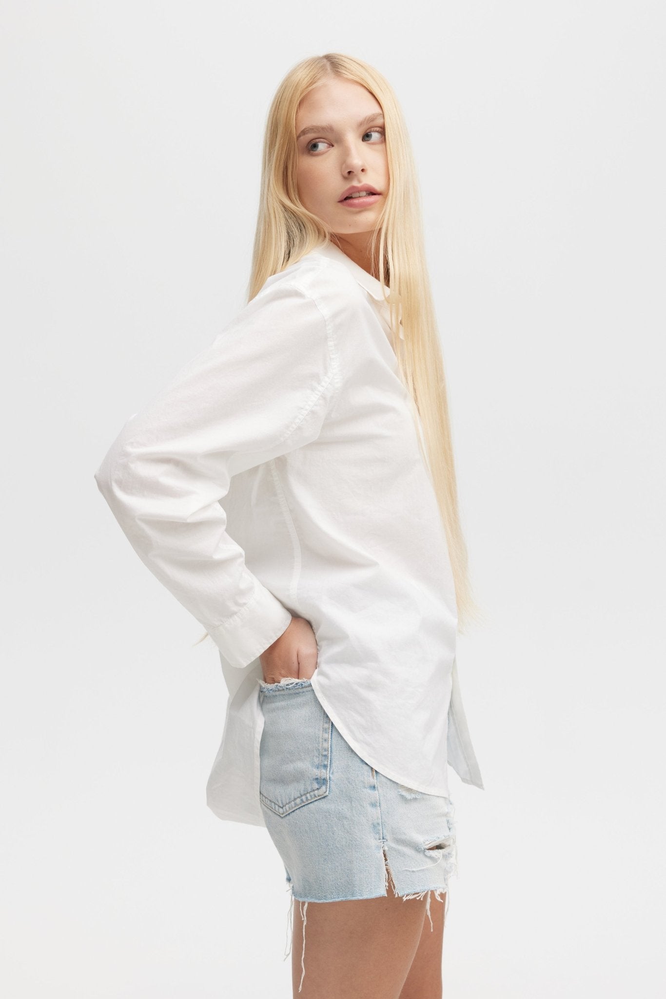 Woman wearing a white blazer over a light blue denim shirt on a white background