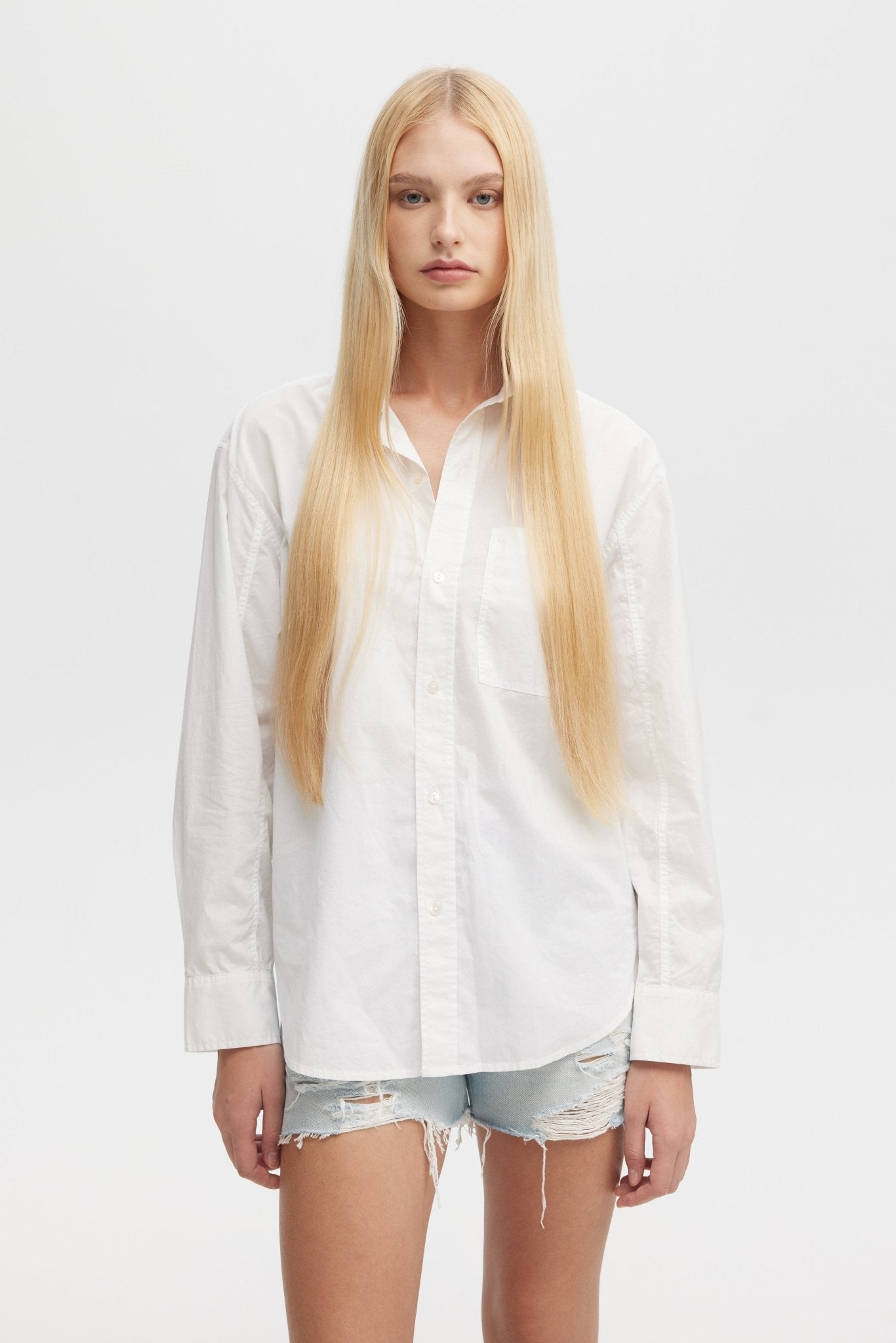 Person wearing a white shirt and denim shorts on a plain background
