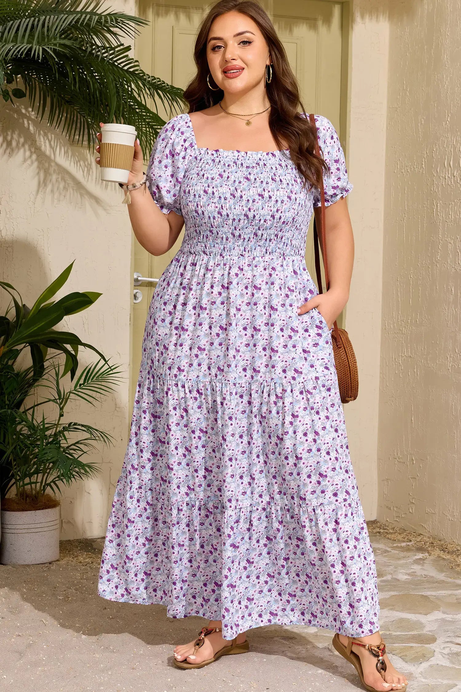 Woman in a floral dress holding a coffee cup outdoors.