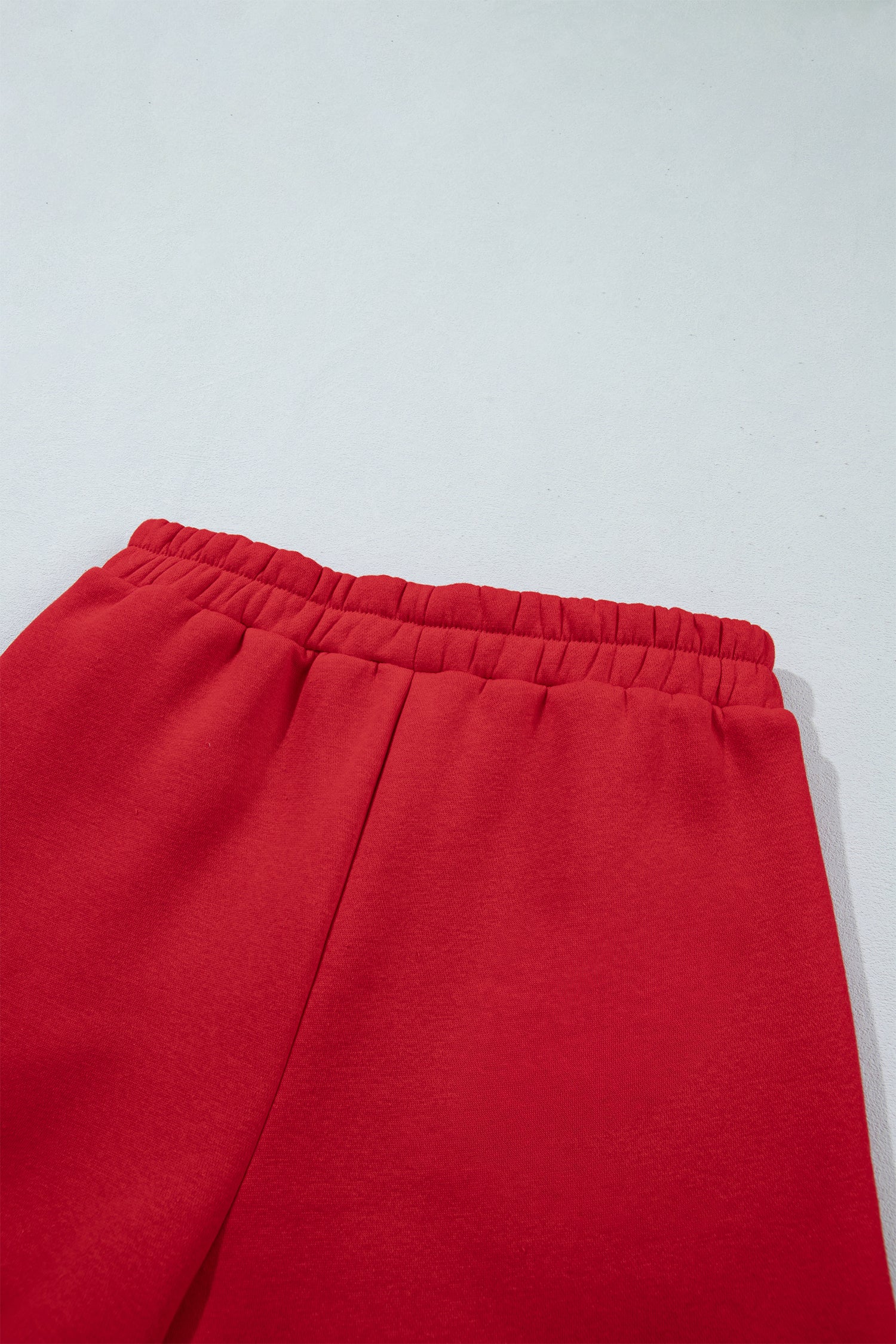 Close-up of bright red sweatpants showing the elastic waistband and upper leg area against a light gray background.