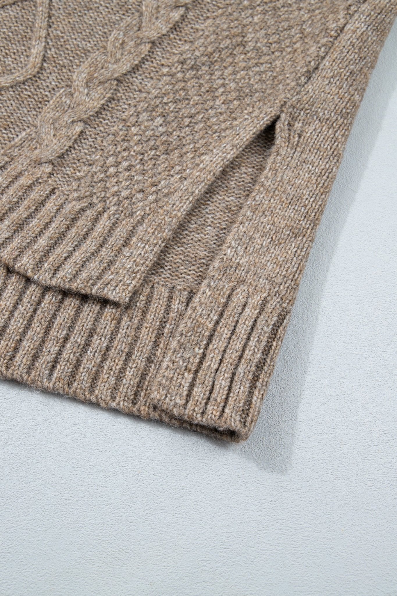 Close-up of taupe knit sweater with cable pattern, ribbed hem, and side slit.