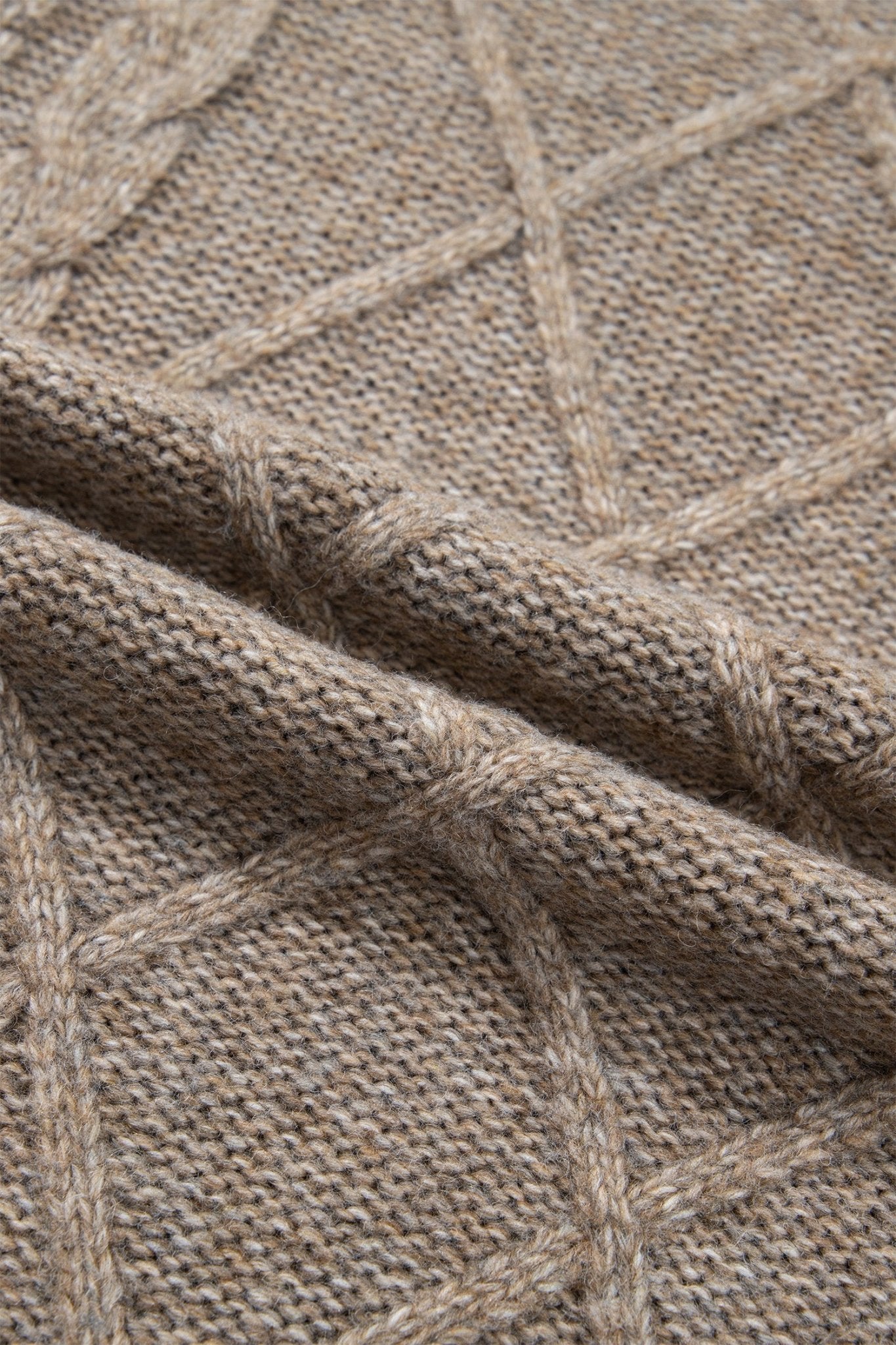 Close-up of warm taupe-beige cable-knit textile with folded fabric layers.