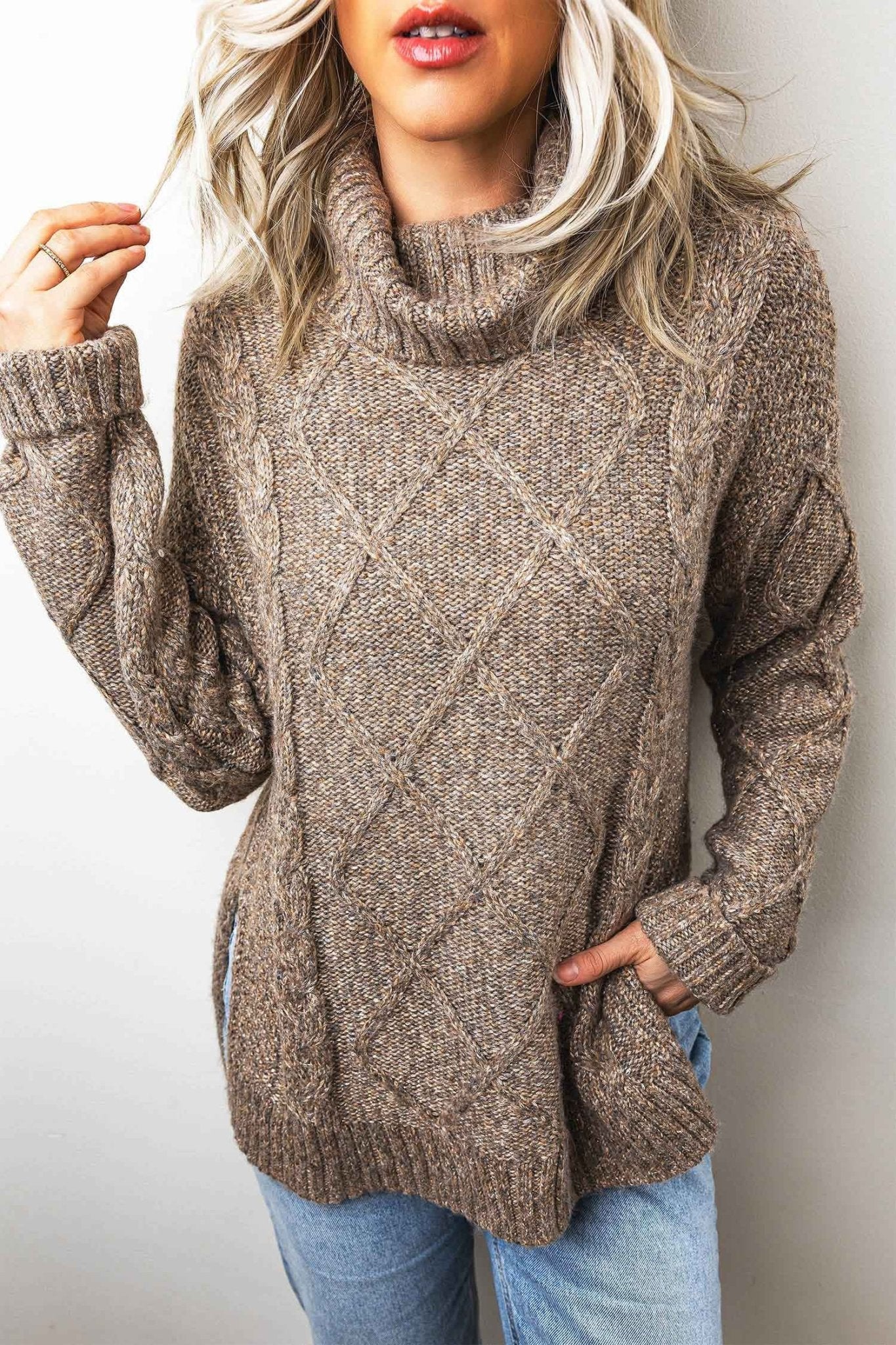 Woman in heathered taupe-brown chunky cowl-neck sweater with light-wash jeans.