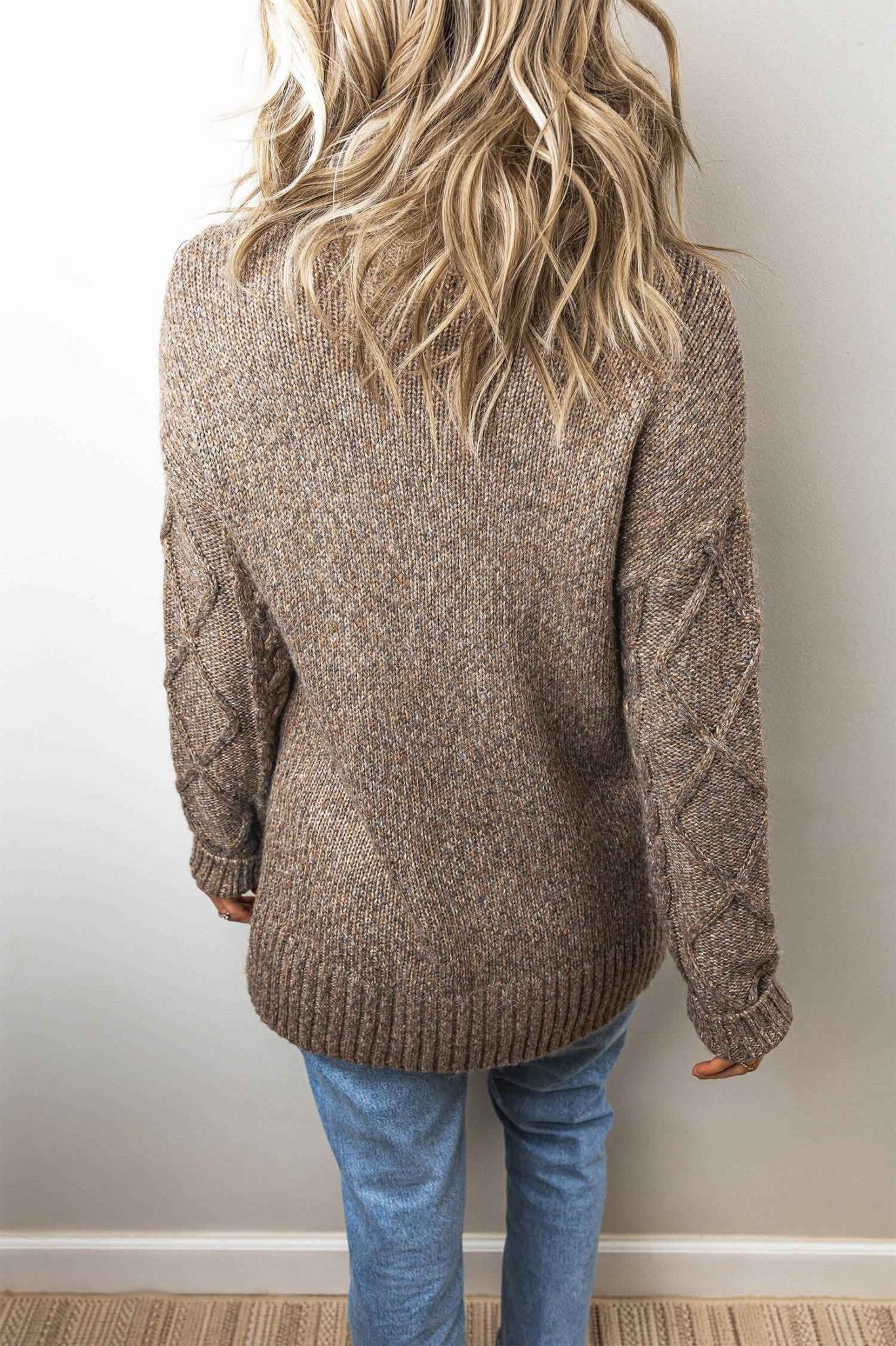 Back view of woman in brown-beige heathered cable-knit sweater and blue jeans.