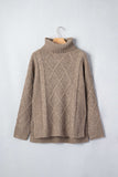 A beige cable-knit turtleneck sweater hanging on a wooden hanger against a light gray wall.