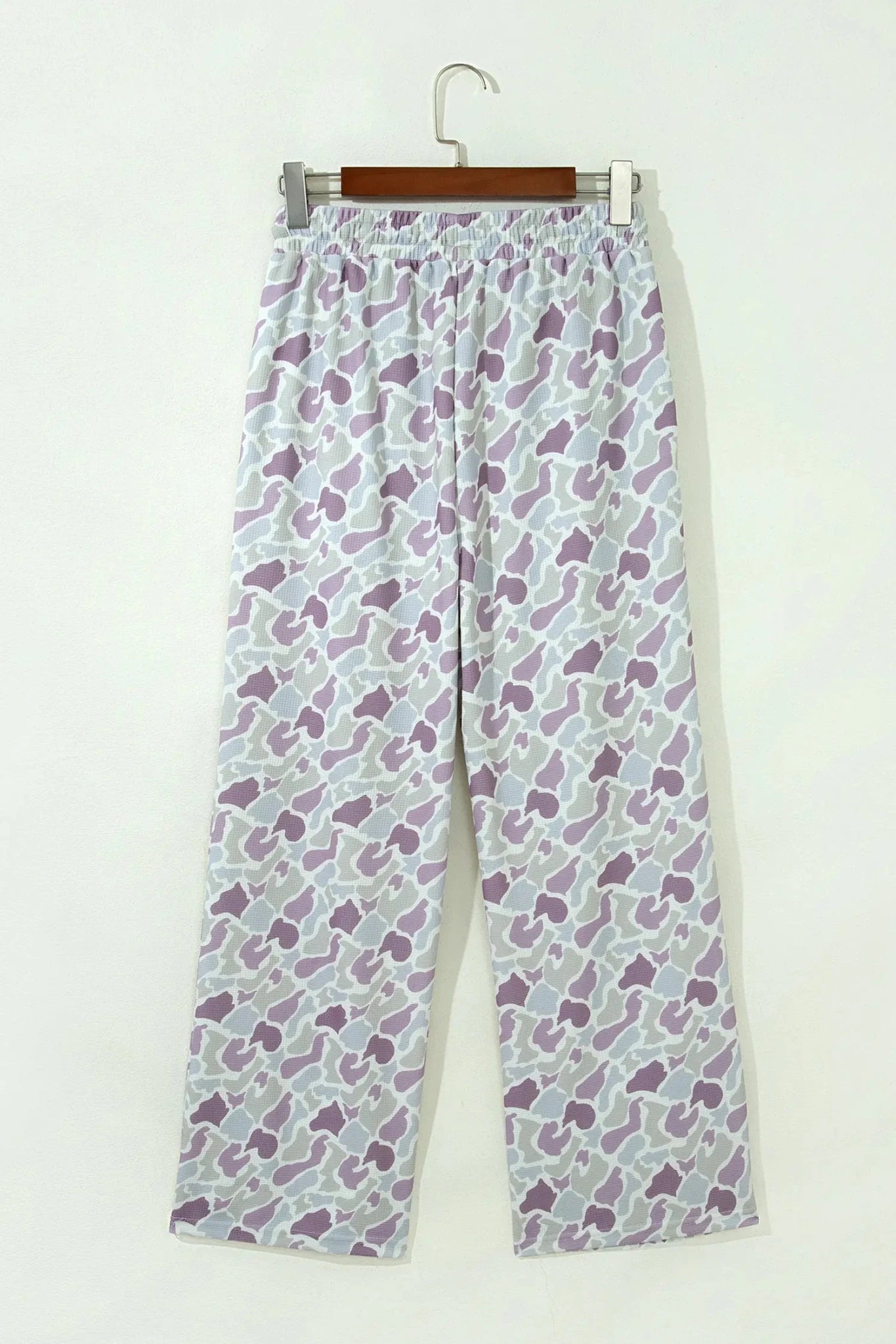 Purple and white abstract wide-leg lounge pants on a wooden hanger.