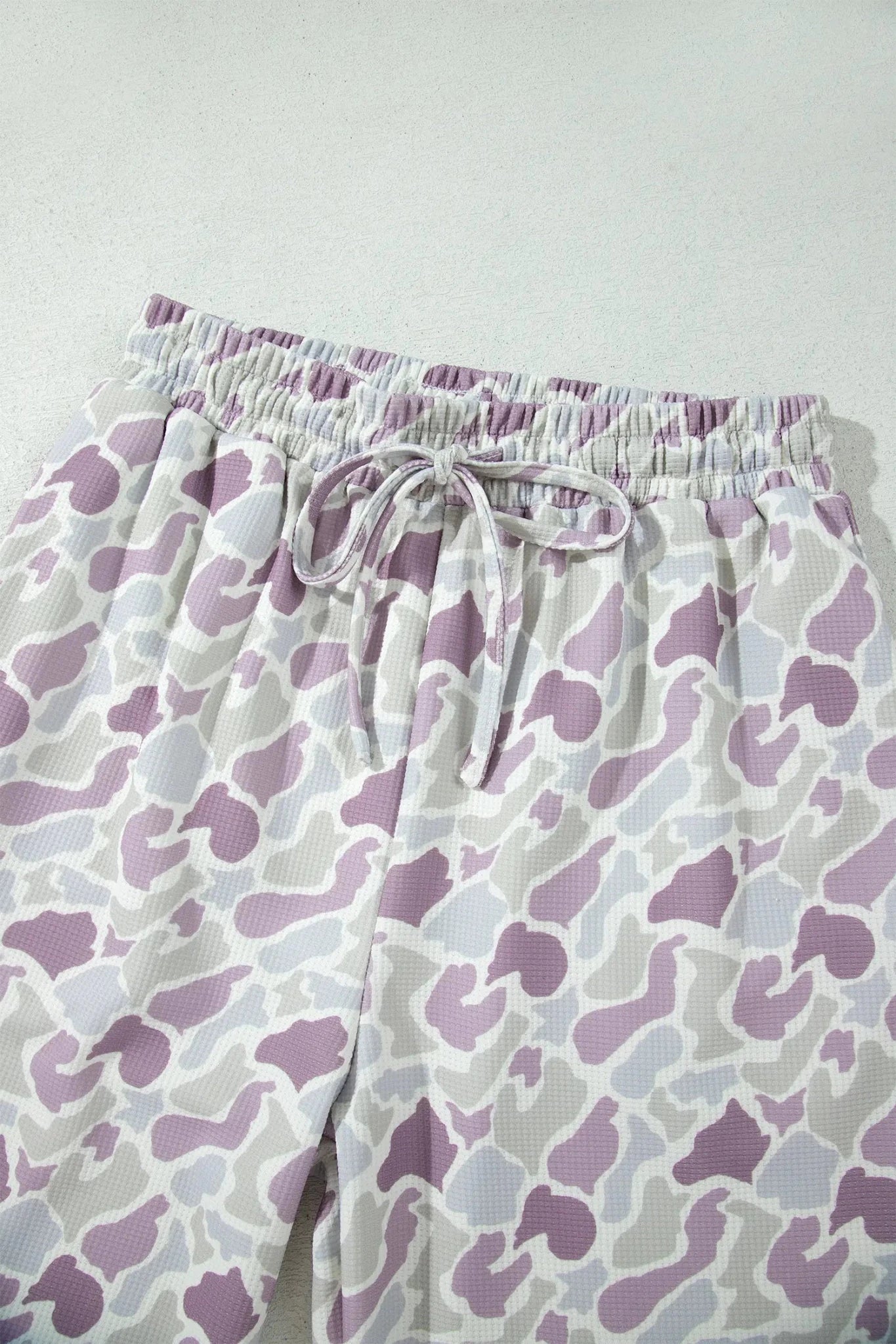 White drawstring shorts with a purple and gray abstract organic pattern, shown on a light gray background.