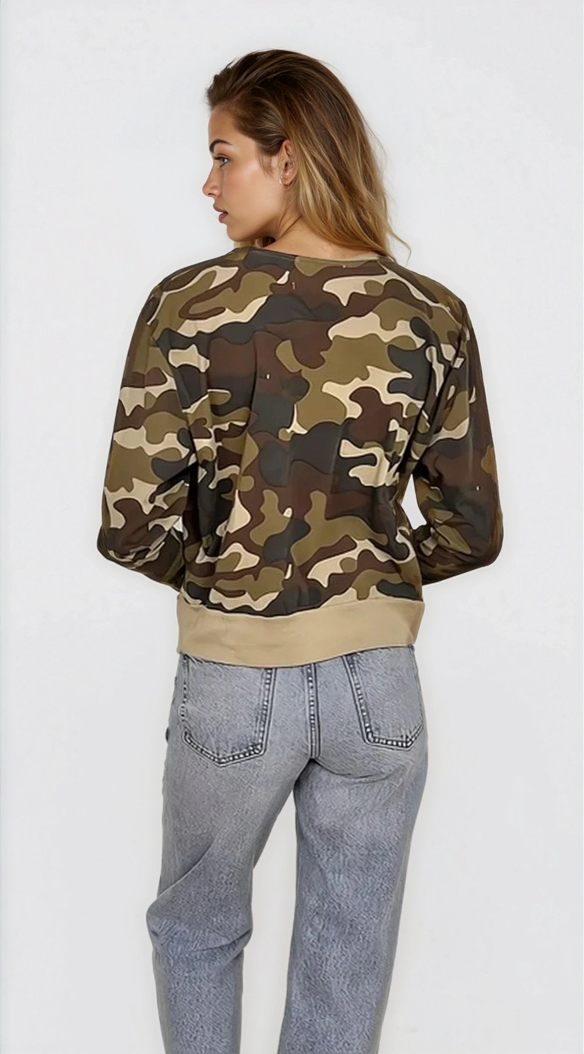 Person wearing a camouflage sweater and light blue jeans on a white background